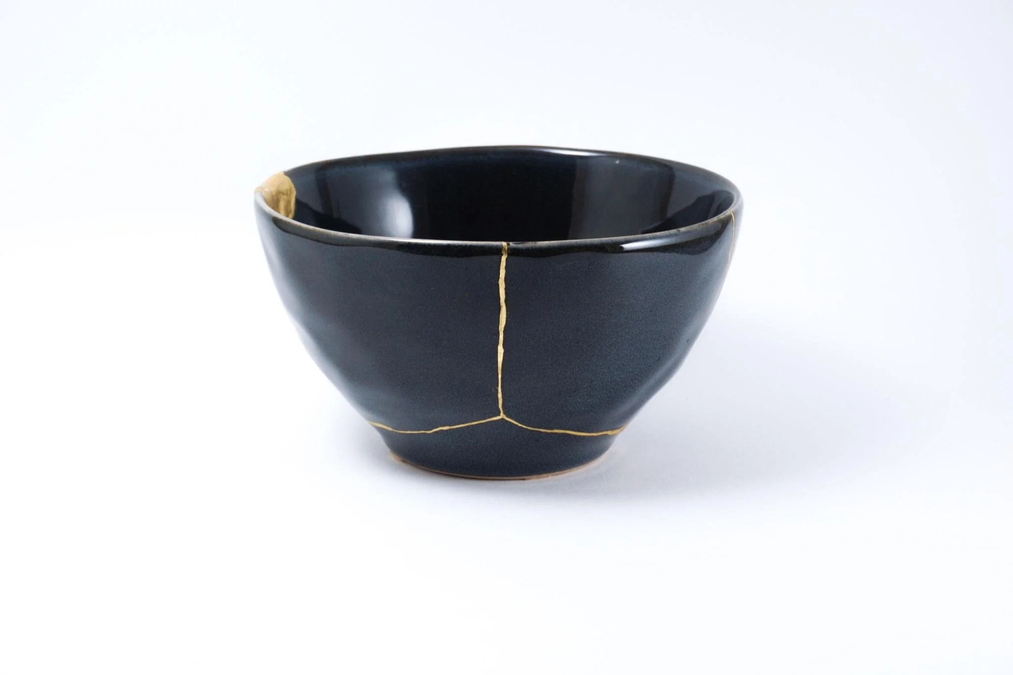 A black ceramic bowl with gold rim and crack lines.