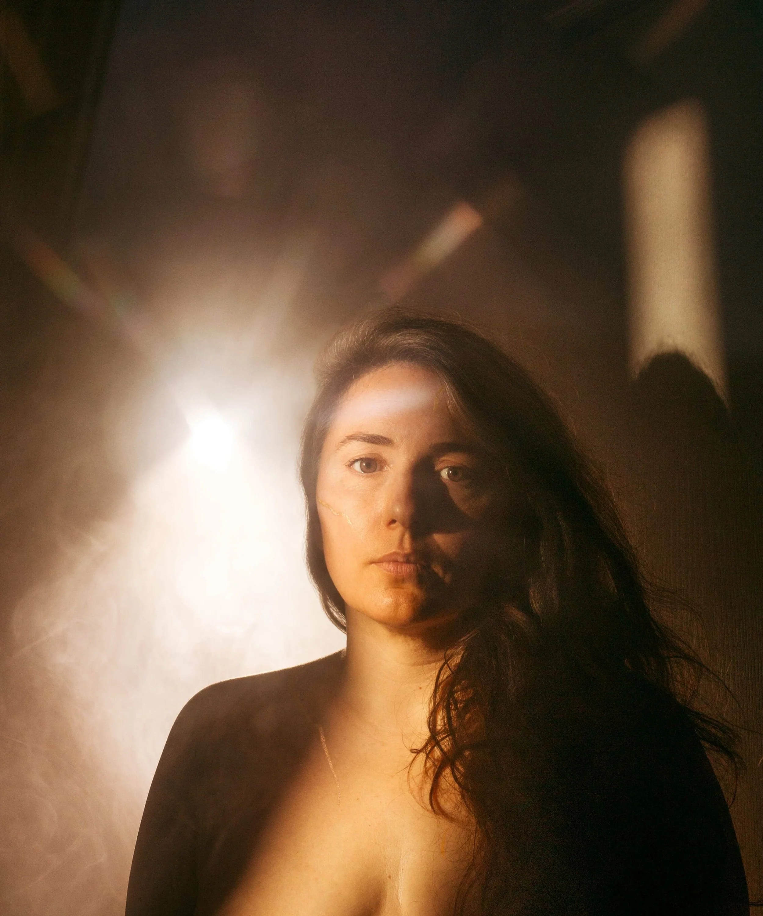 Portrait d'une jeune femme avec lumière douce et ambiance sombre, cheveux longs, regard tranquille.