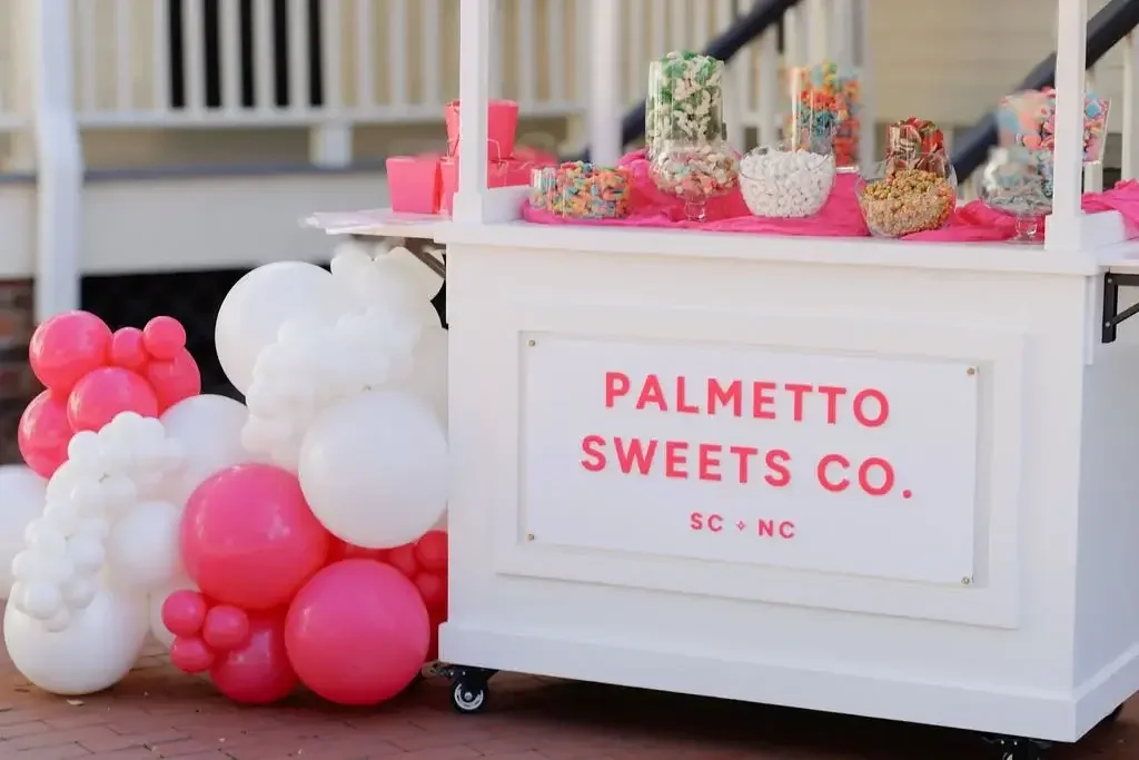 Palmetto Sweets Co. white candy cart with pink and white balloon garland decoration and glass containers filled with assorted candies for Charlotte NC events