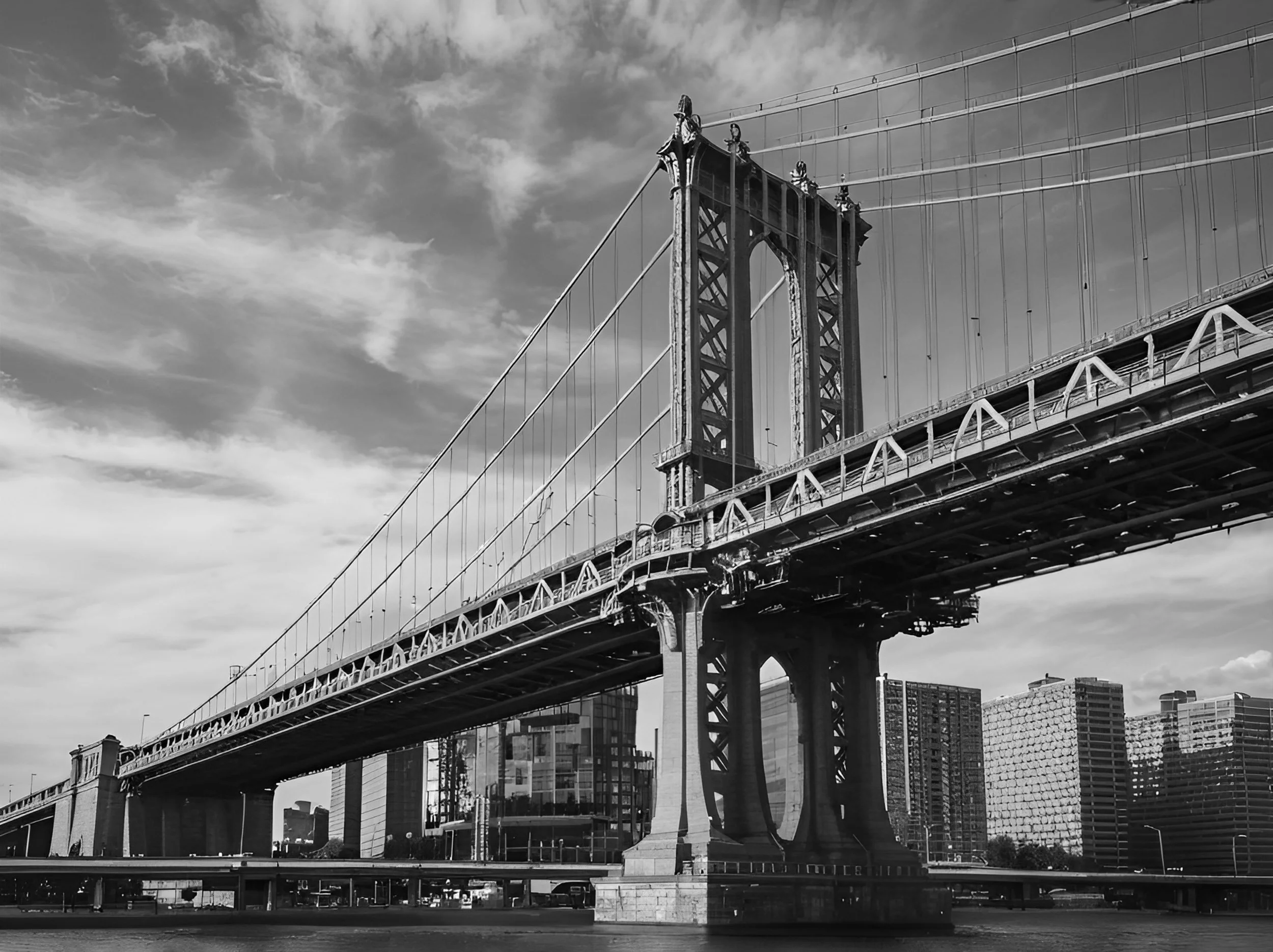 Le pont de Brooklyn à New York en noir et blanc, avec des bâtiments en arrière-plan et un ciel partiellement nuageux.