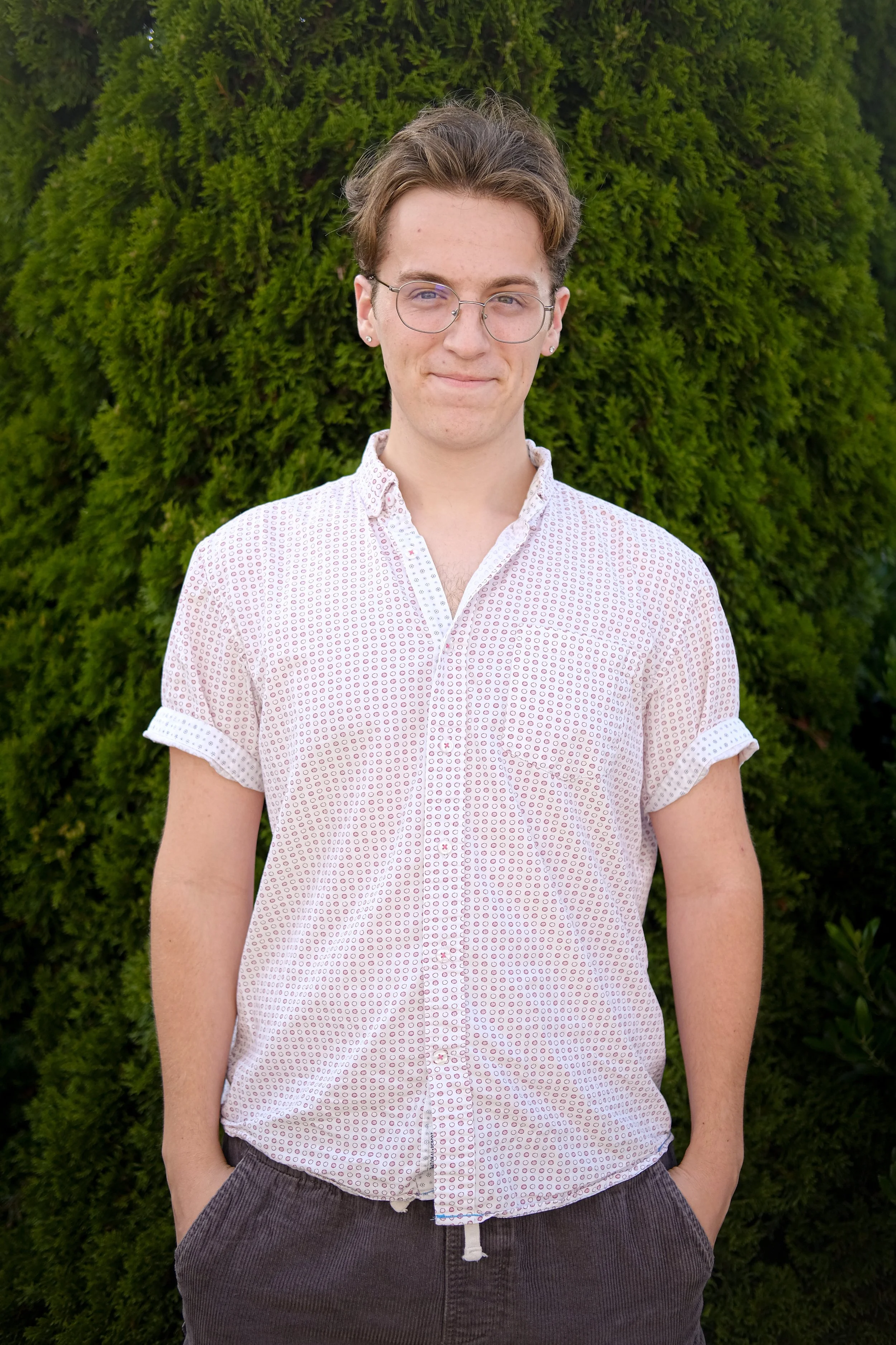 Person in white button-up shirt standing in front of green foliage.
