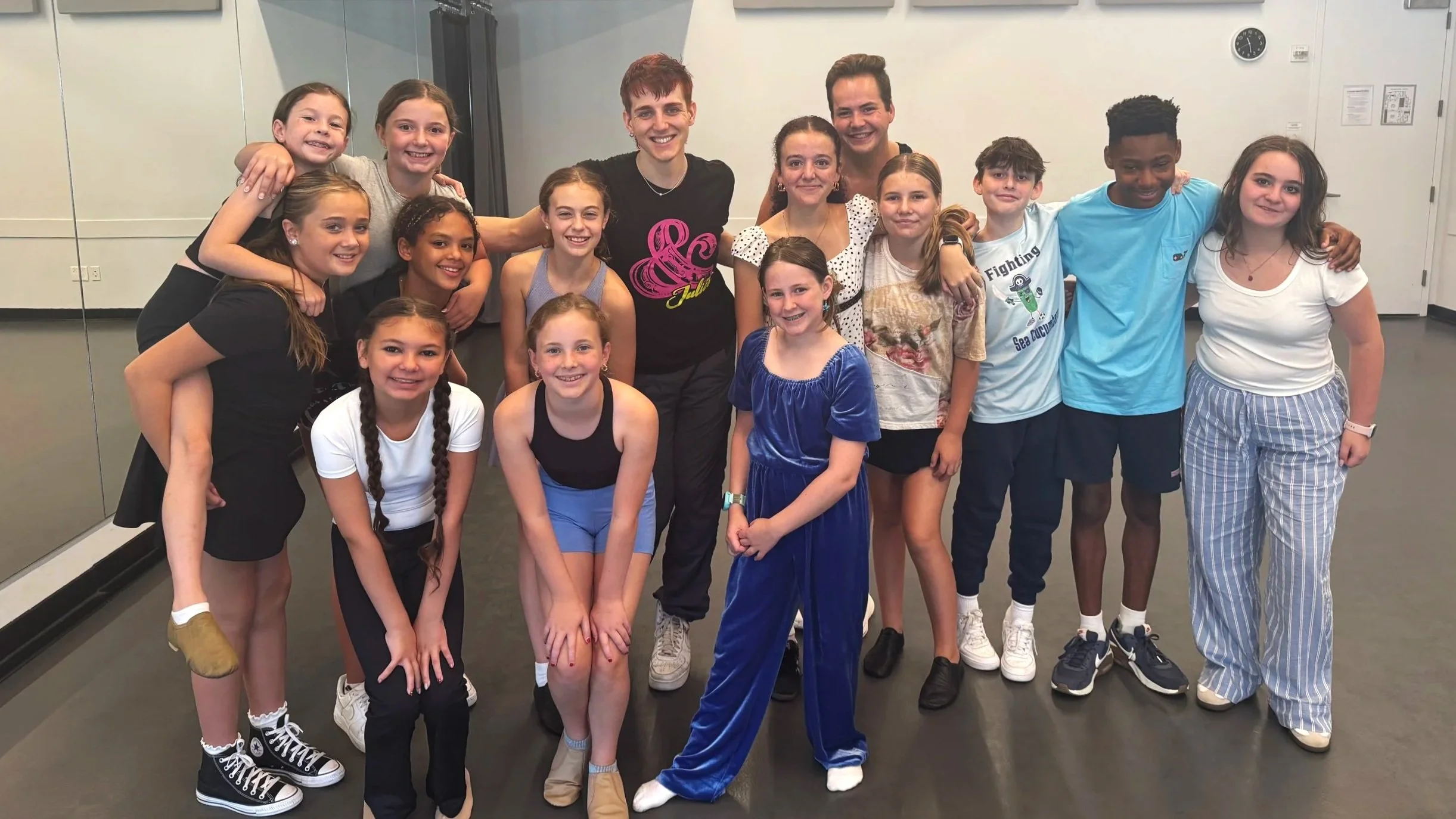 Group of children and two adults posing in a dance studio.