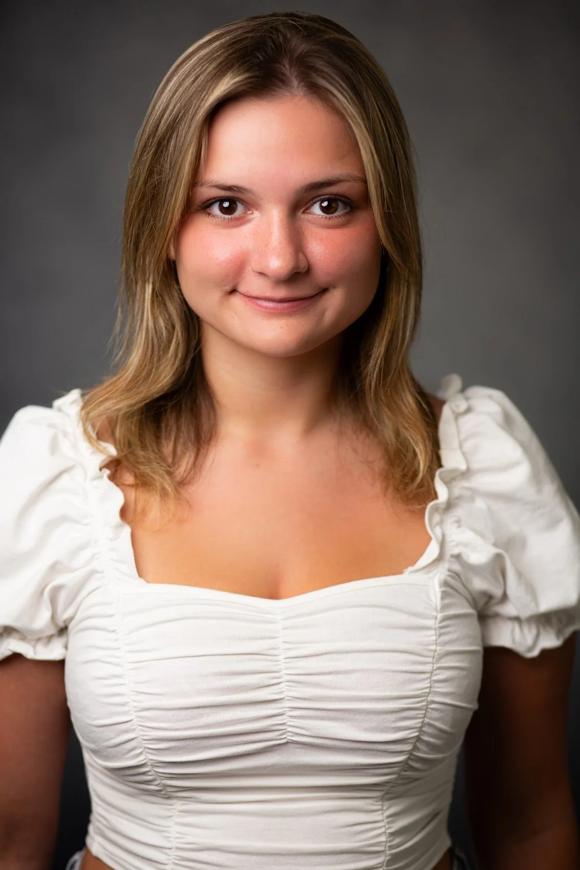 A woman with long, wavy blonde hair and blue eyes, wearing a black sleeveless top, looking at the camera with a slight smile.