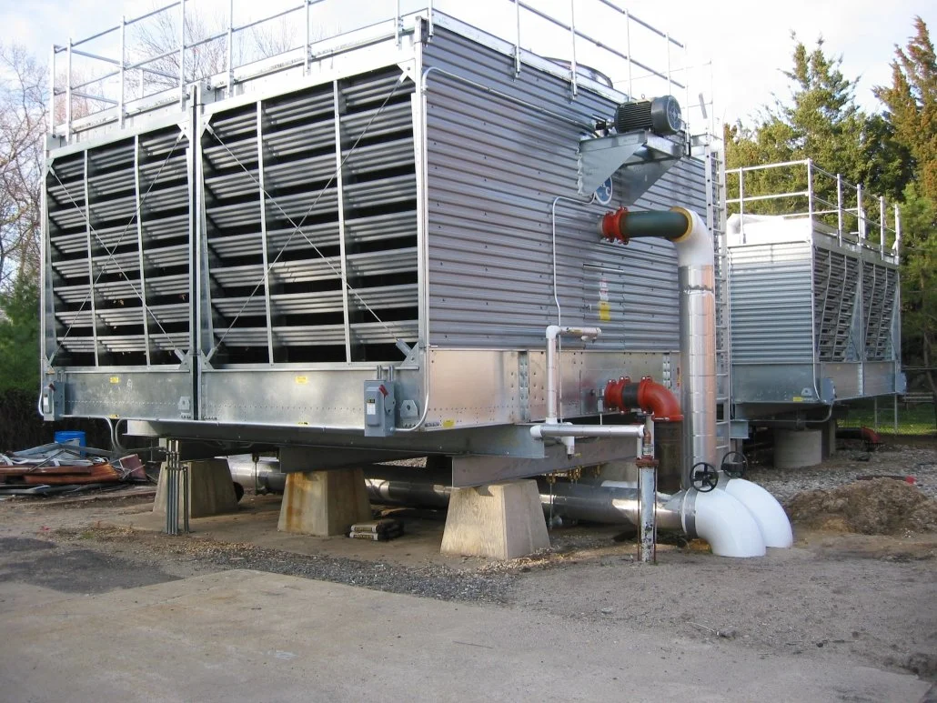 Industrial cooling or HVAC unit with metal panels, pipes, and vents, elevated on concrete blocks outdoors.