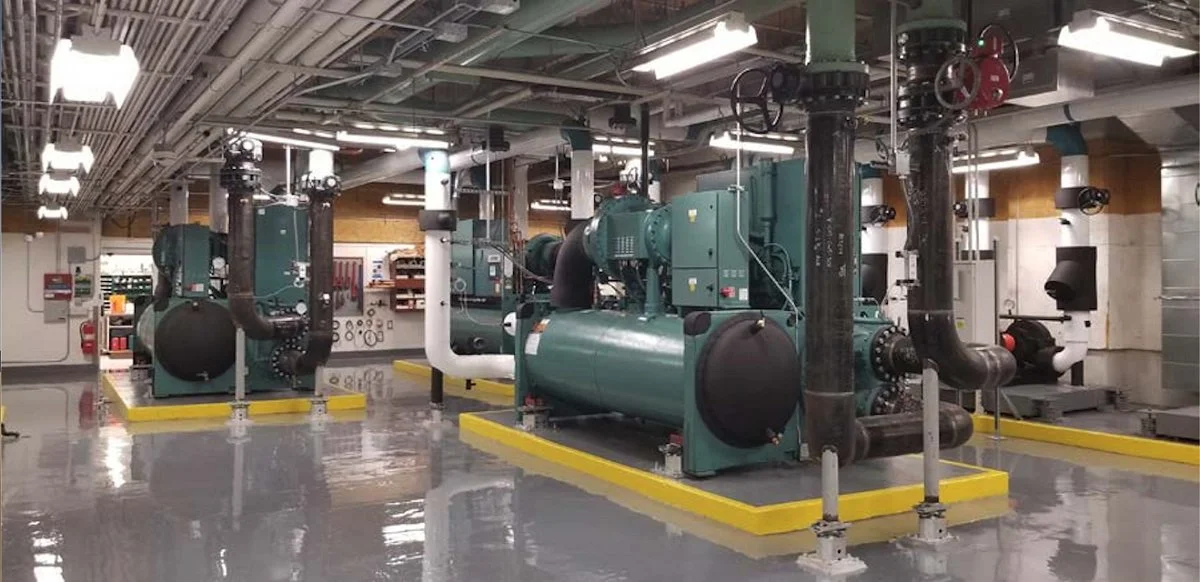 Industrial boiler system with multiple large green machines, black pipes, and control panels in a clean, well-lit room.