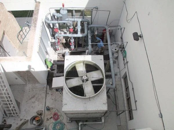 An outdoor rooftop HVAC unit with large fan, pipes, and a technician working nearby.