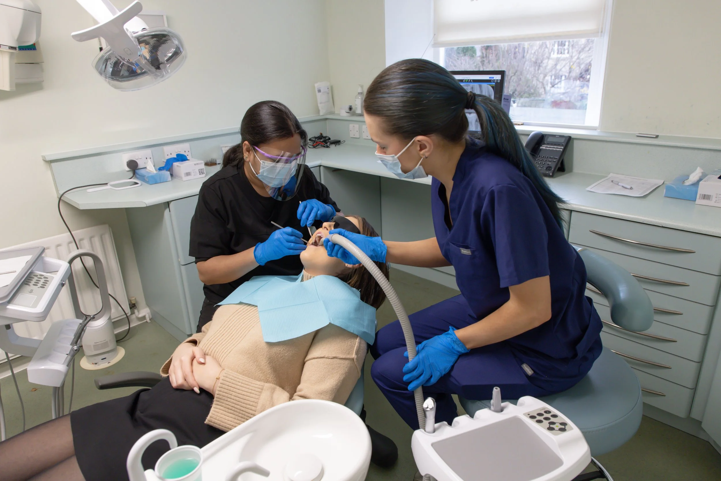 Dentist and dental assistant perform a dental procedure on a patient lying in the dental chair, with dental tools and equipment in the clinic.