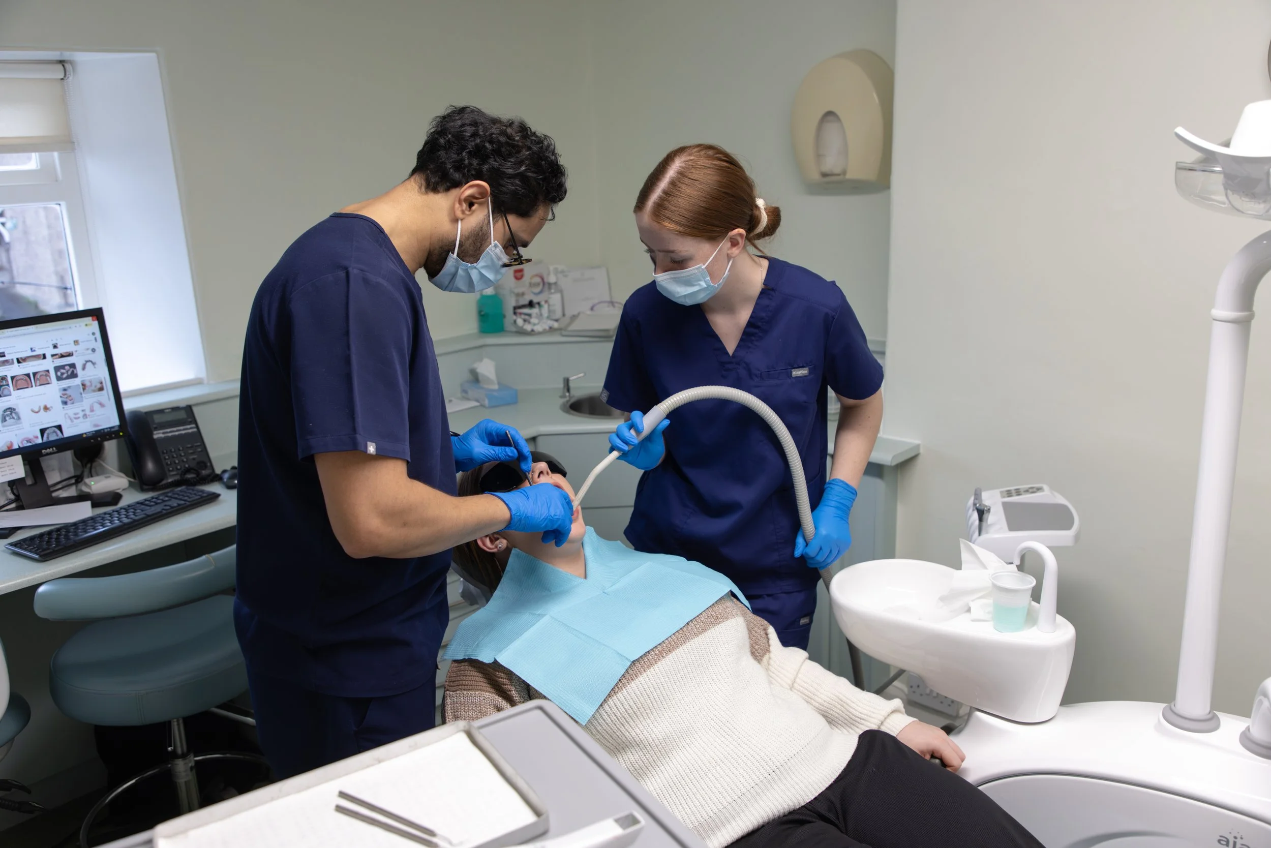 Dentist and dental assistant performing a dental procedure on a female patient in a dental clinic.