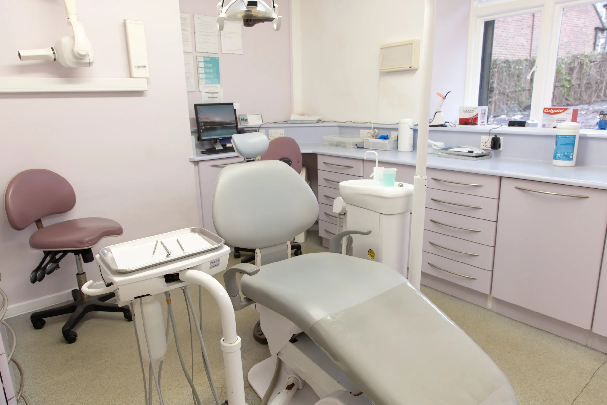 Dental exam room with dental chair, dentist's tools, computer, and dental supplies.