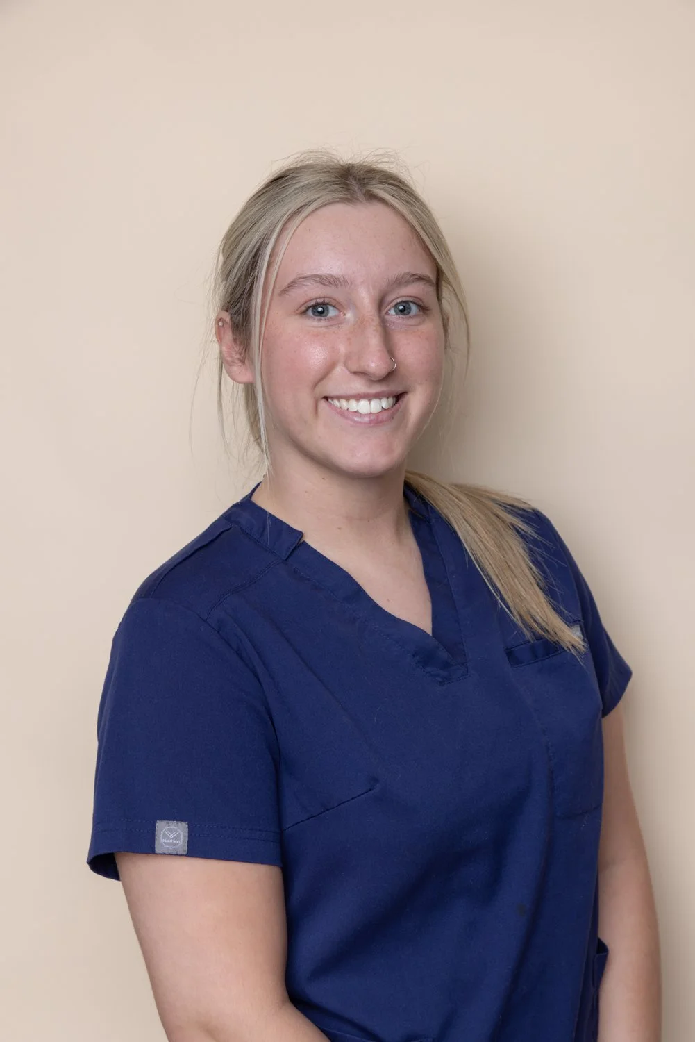 A woman in navy medical scrubs smiling against a beige background.