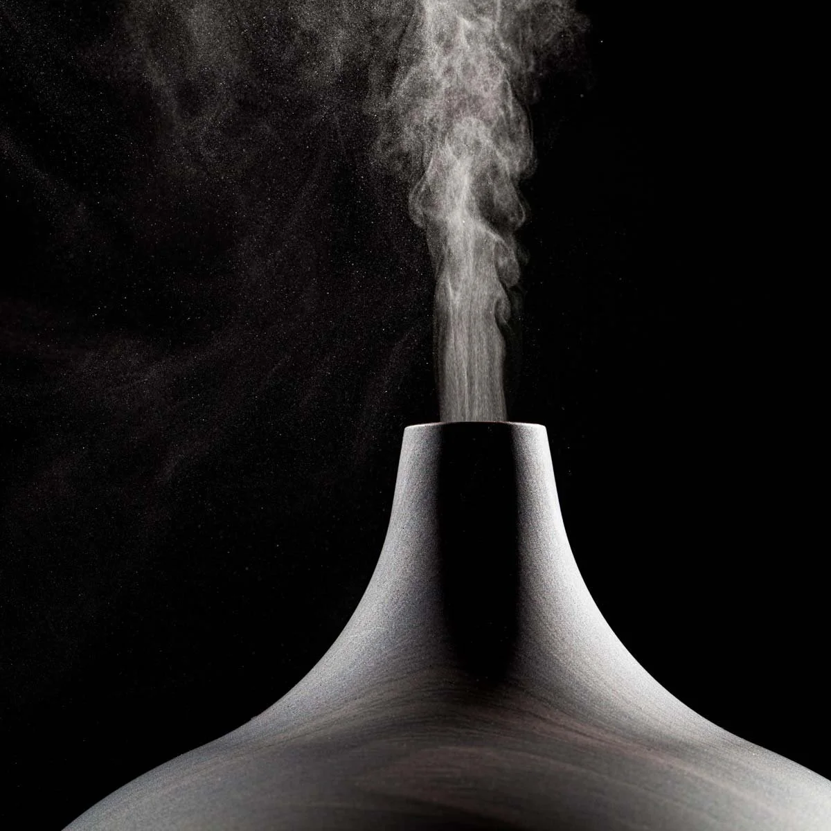 An industrial smokestack emitting white steam or smoke against a dark background.