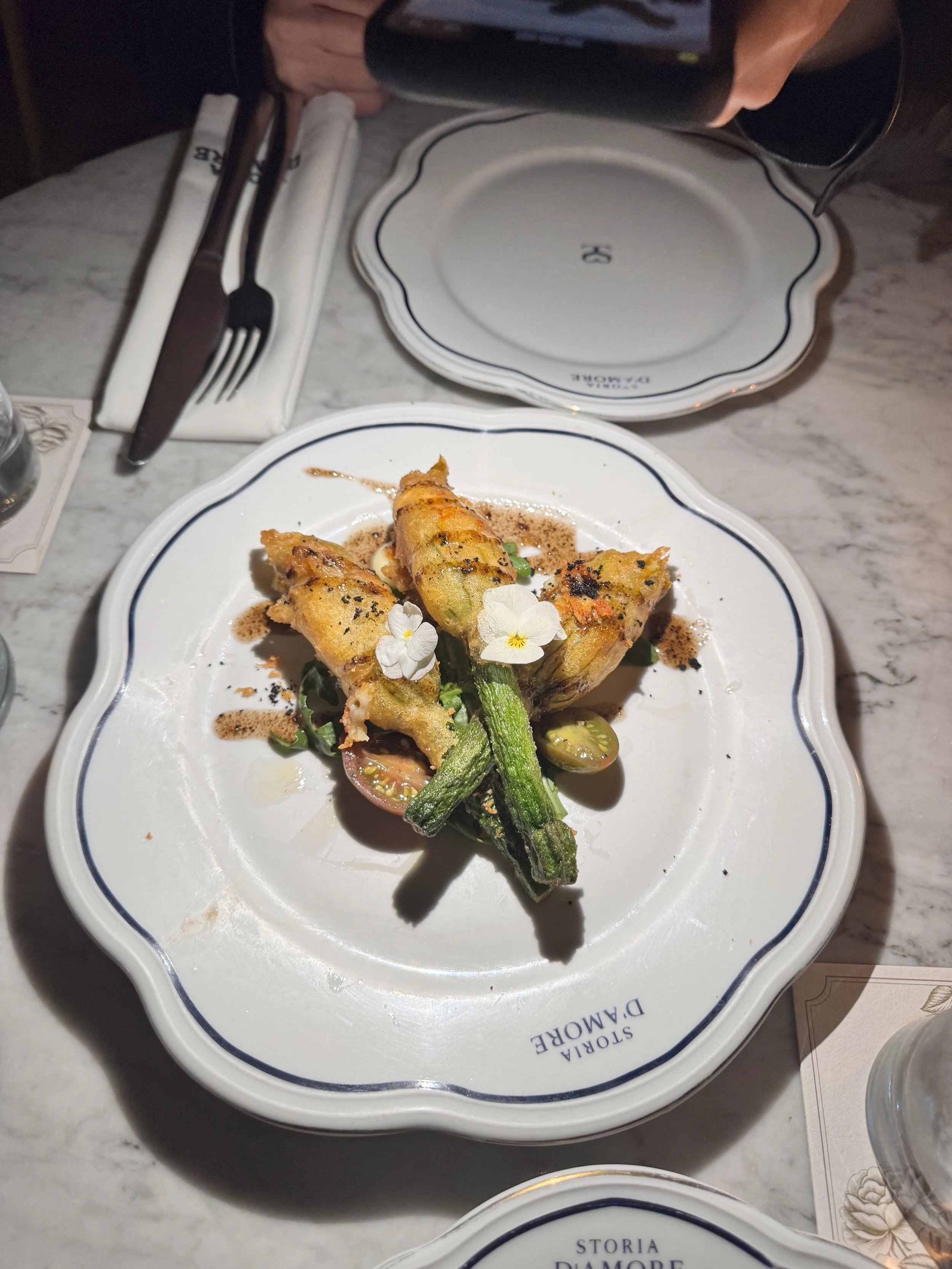 Fried zucchini blossoms garnished with edible flowers and cherry tomatoes on a decorative white plate