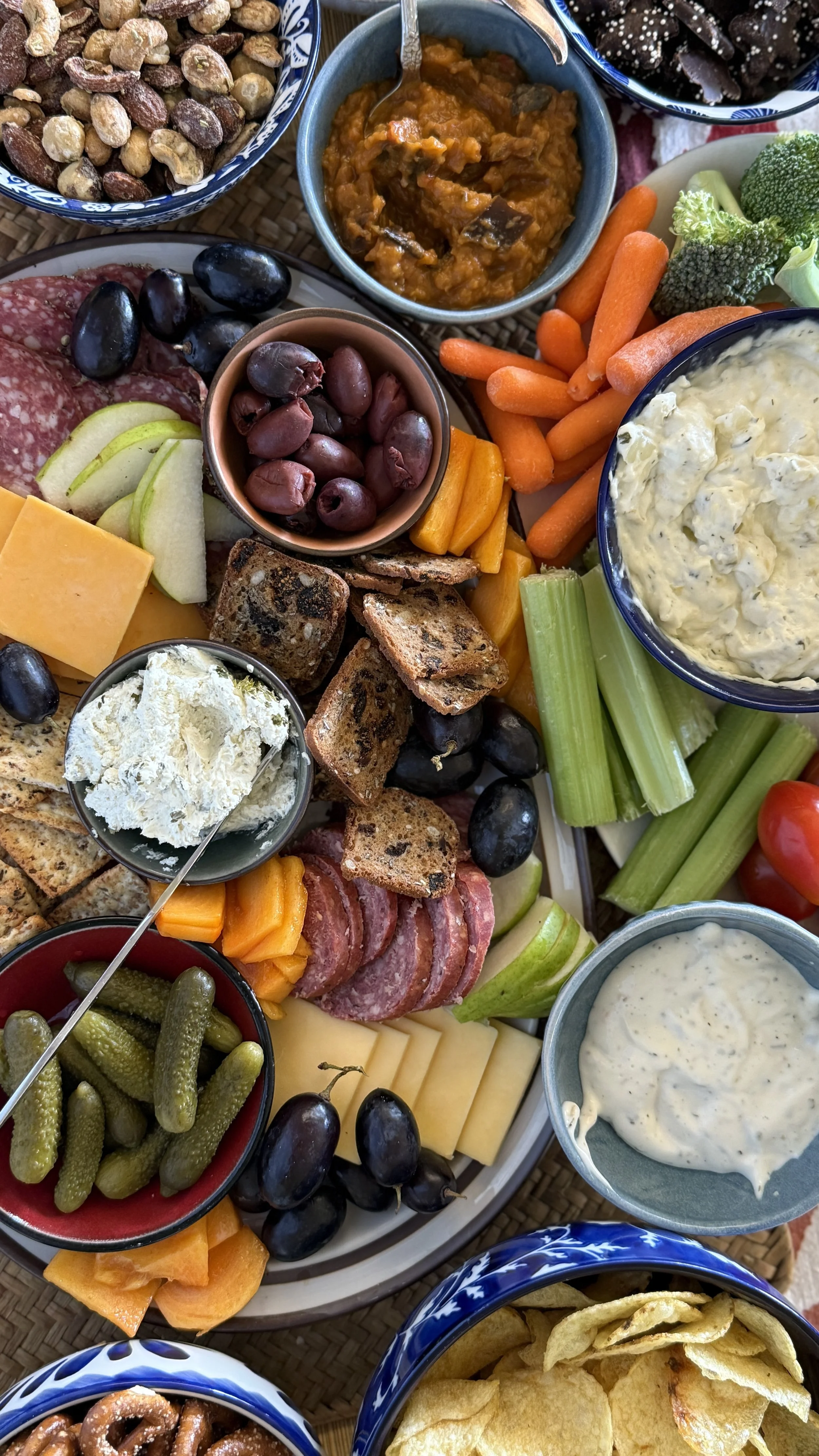 A charcuterie board with various cheeses, grapes, vegetables, dips, crackers, and nuts.