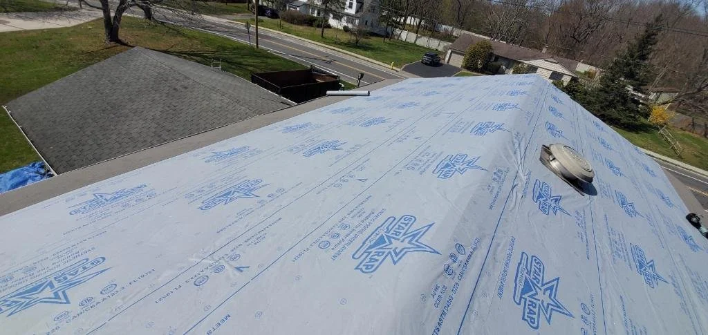 A roof under construction with a layer of weatherproofing material and a vent pipe installed.