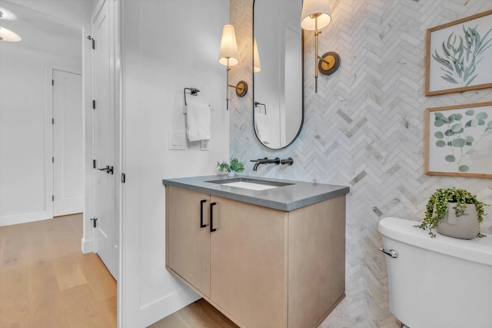Powder room with a floating wood vanity, herringbone tile, and brass sconces
