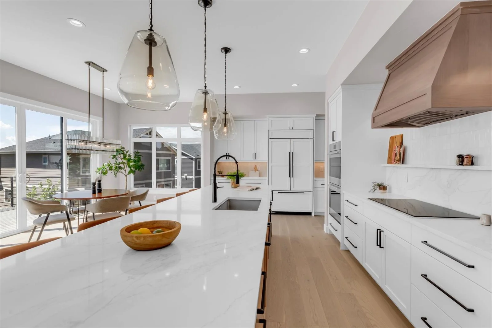 Kitchen island with a white countertop, black faucet, glass pendants, and wood range hood
