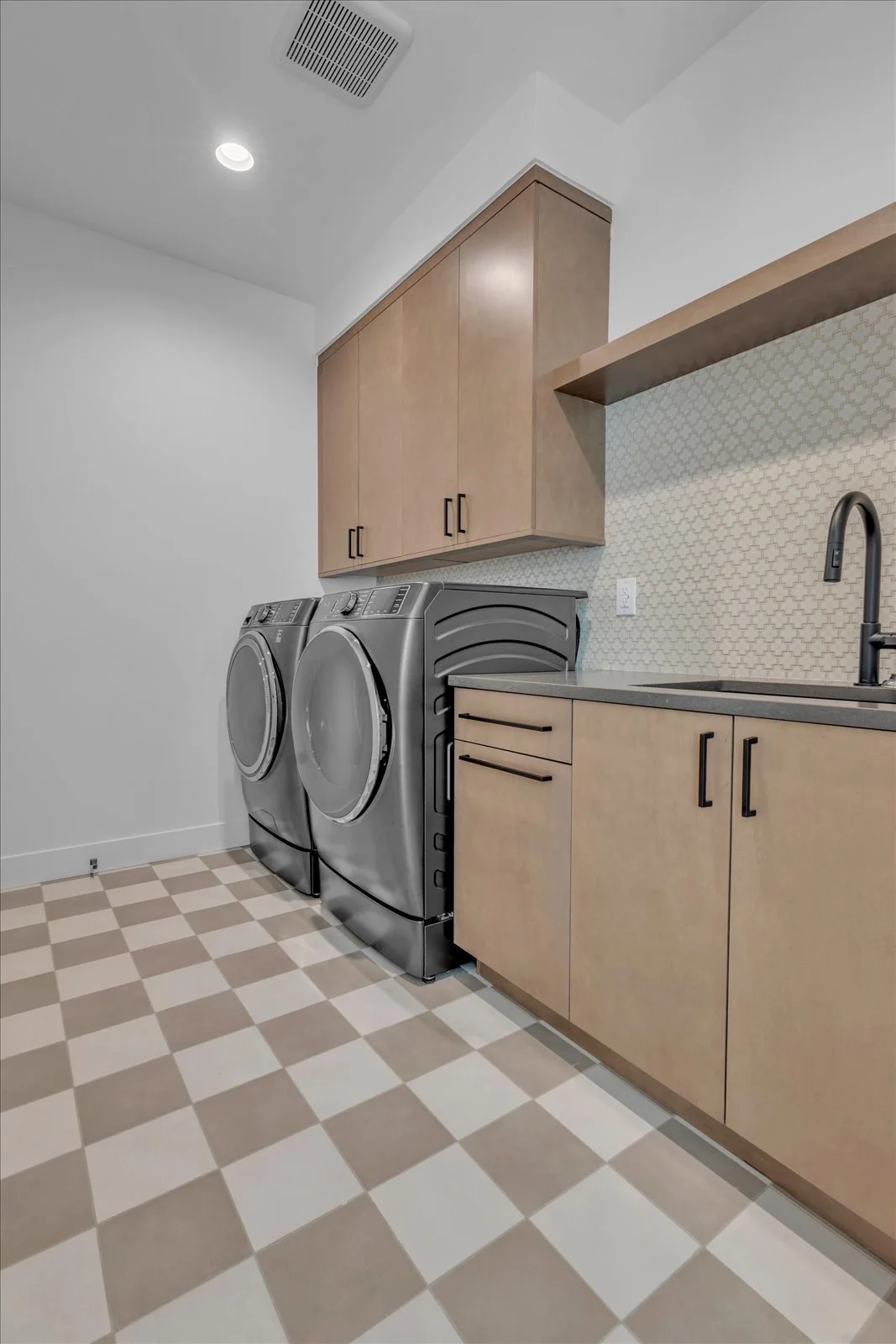 Laundry room with wood cabinetry, a sink, front-loading appliances, and a checkerboard floor