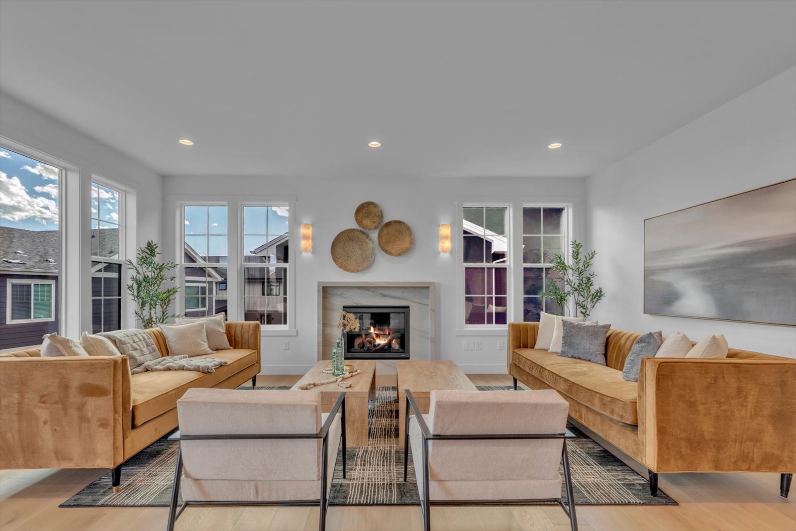 Living room with golden sofas, cream chairs, and a fireplace between tall windows