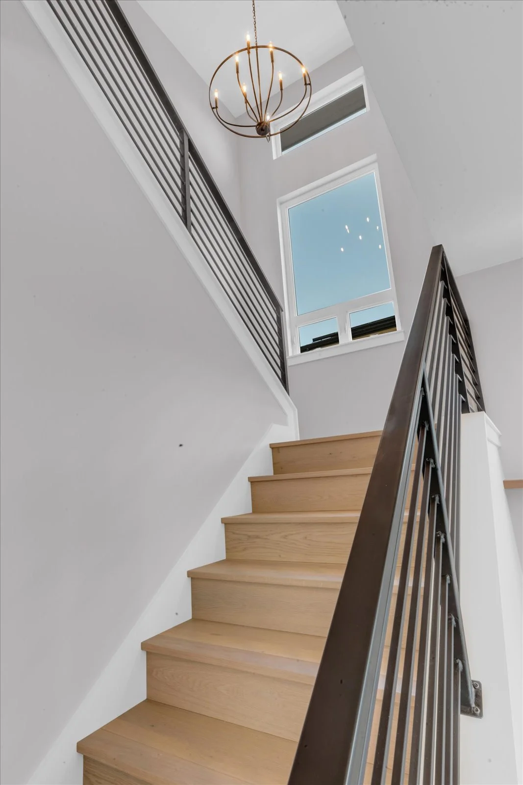 Wood staircase with black railings, tall windows, and a round chandelier
