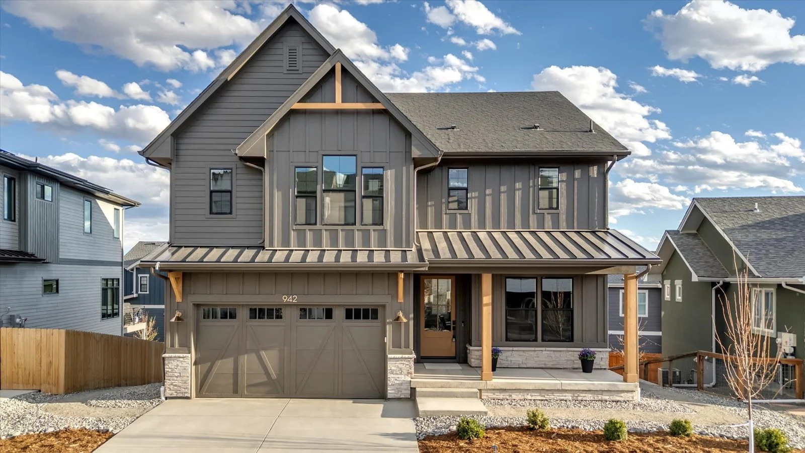 Front exterior of a gabled home with gray siding, timber porch posts, and a double garage