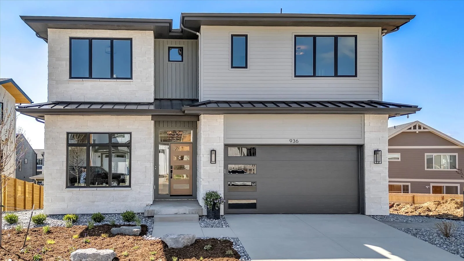Front exterior of a two-story home with pale stone, gray siding, and a dark garage door