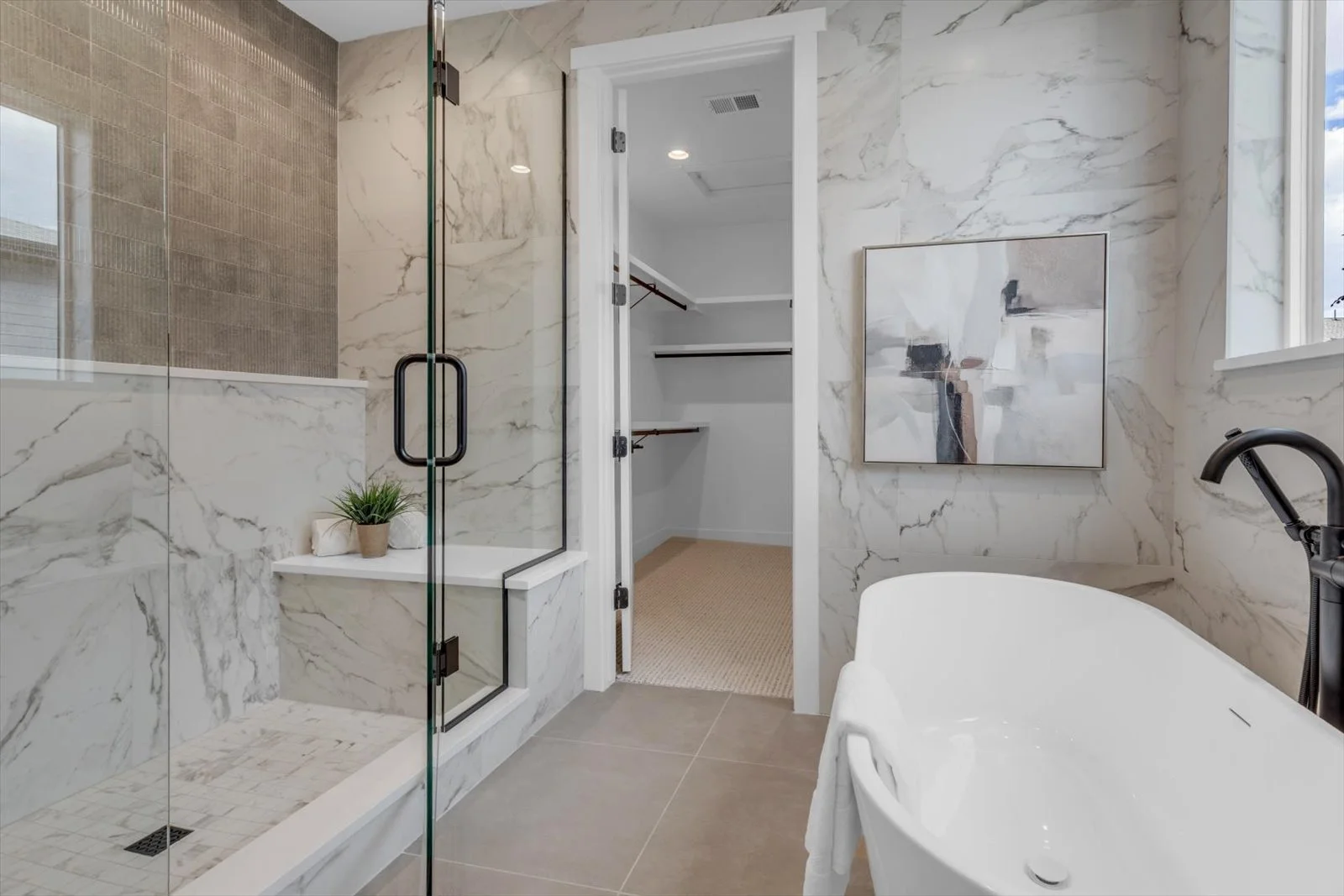 Freestanding bathtub beside a glass shower with veined tile walls