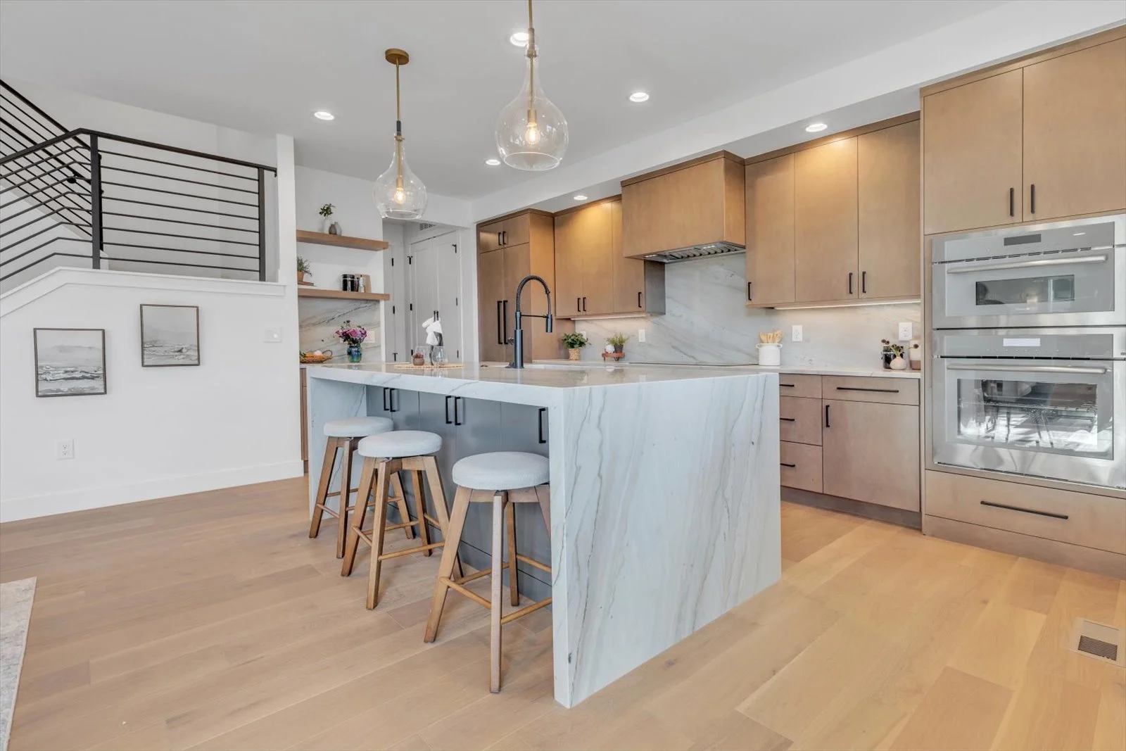 Kitchen with wood cabinetry, a waterfall island, glass pendants, and black hardware