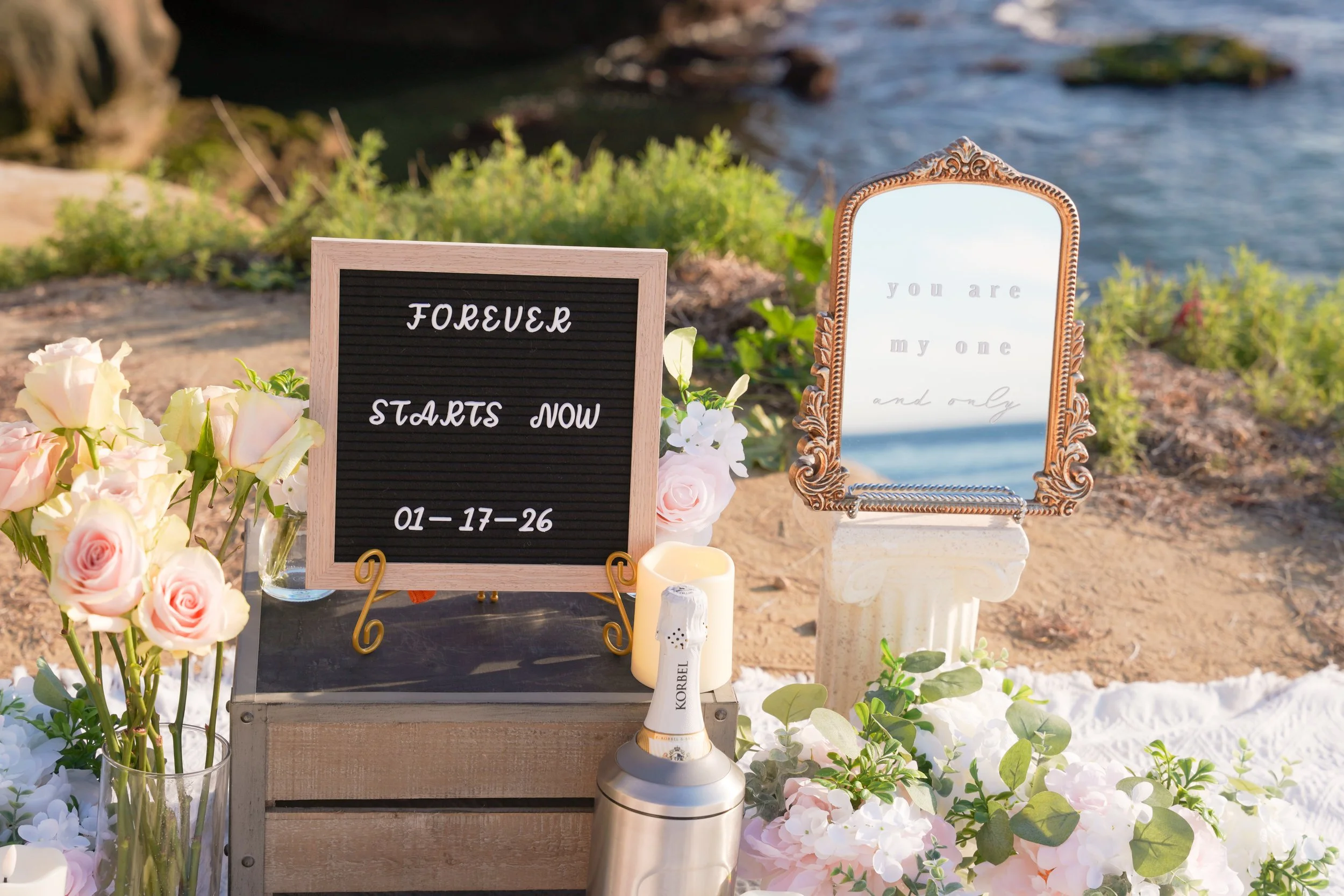 Minimal boho proposal decor featuring neutral textiles, floral accents, and wine styled for an intimate outdoor surprise proposal