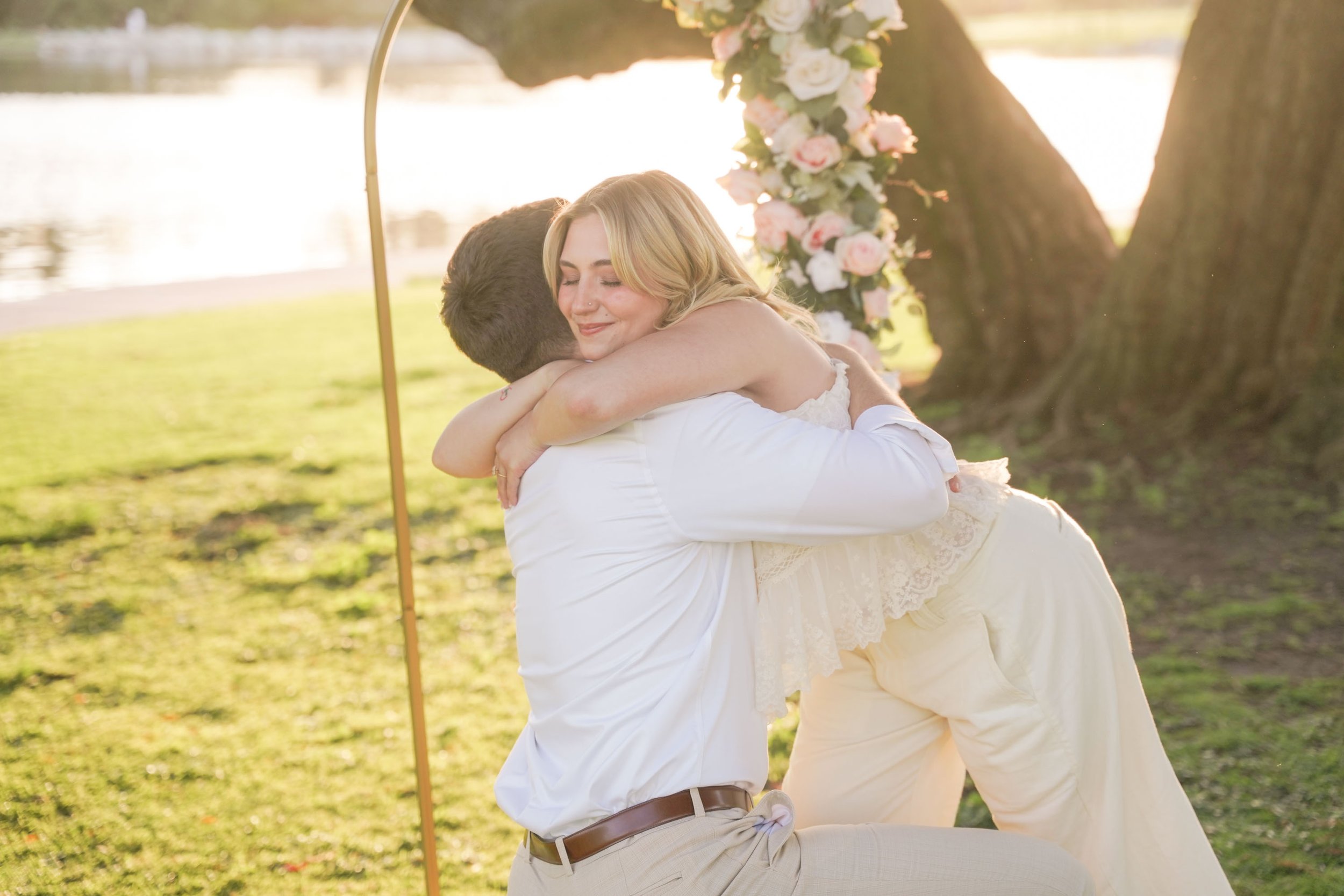 Orange County surprise proposal photographer capturing couple embracing after proposal under willow trees at sunset with signature yes arch setup