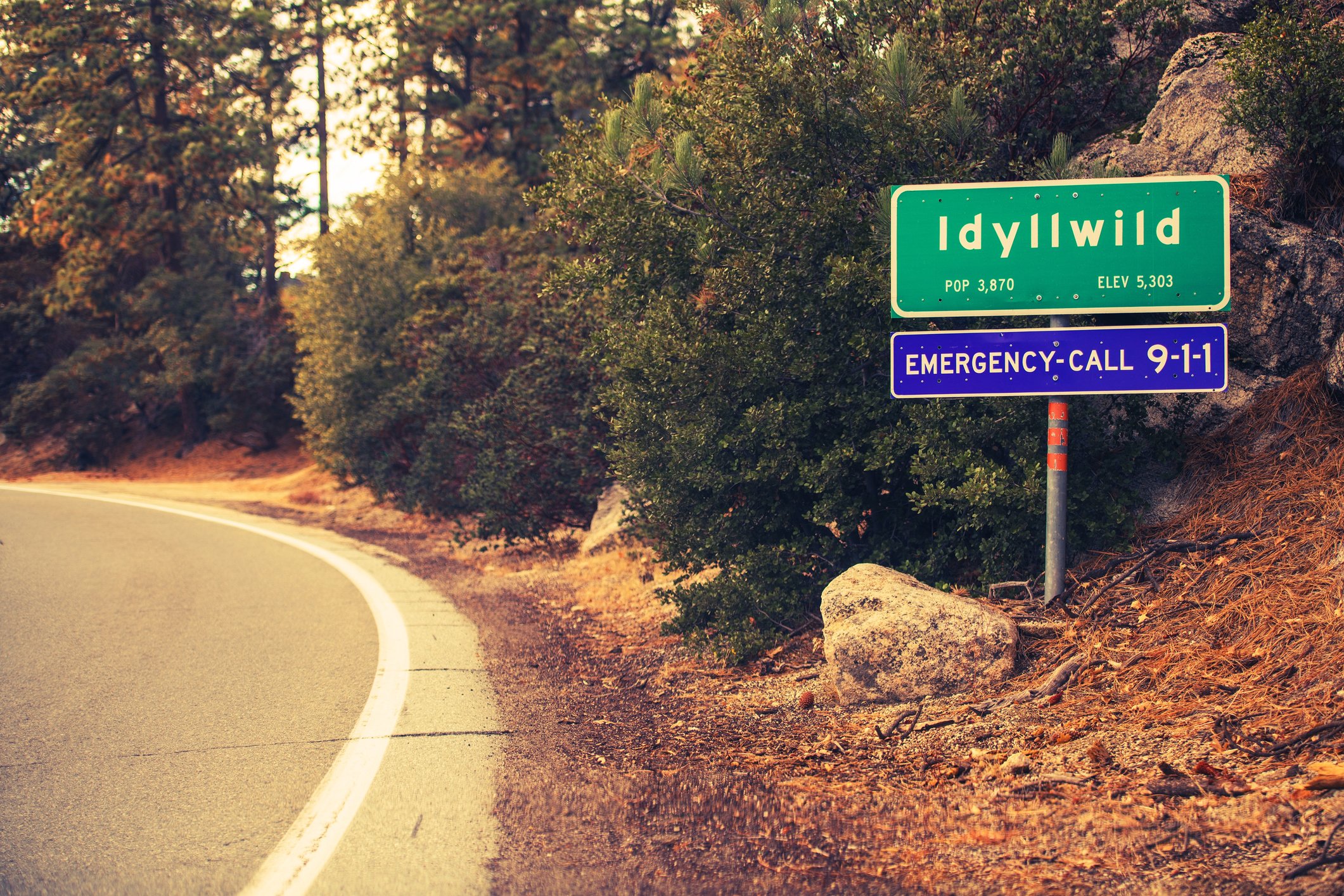 View of the Idyllwild welcome sign surrounded by pine trees and rocky mountain terrain, captured while driving up from the southern entrance—marking the start of a peaceful escape into the mountains. Book your Idyllwild milestone or adventure sessio
