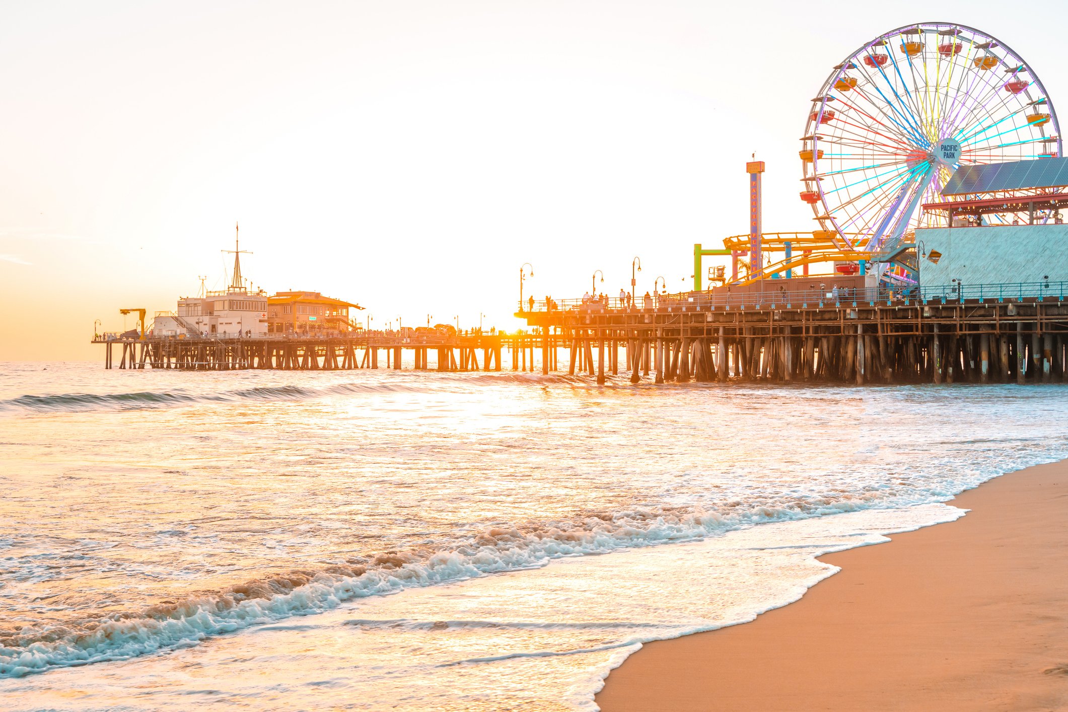 Santa Monica Pier at sunset with the Ferris wheel glowing, waves crashing along the shore, and golden light reflecting off the ocean—ideal setting for a playful and romantic photo session. Book your Santa Monica milestone or couples shoot today.