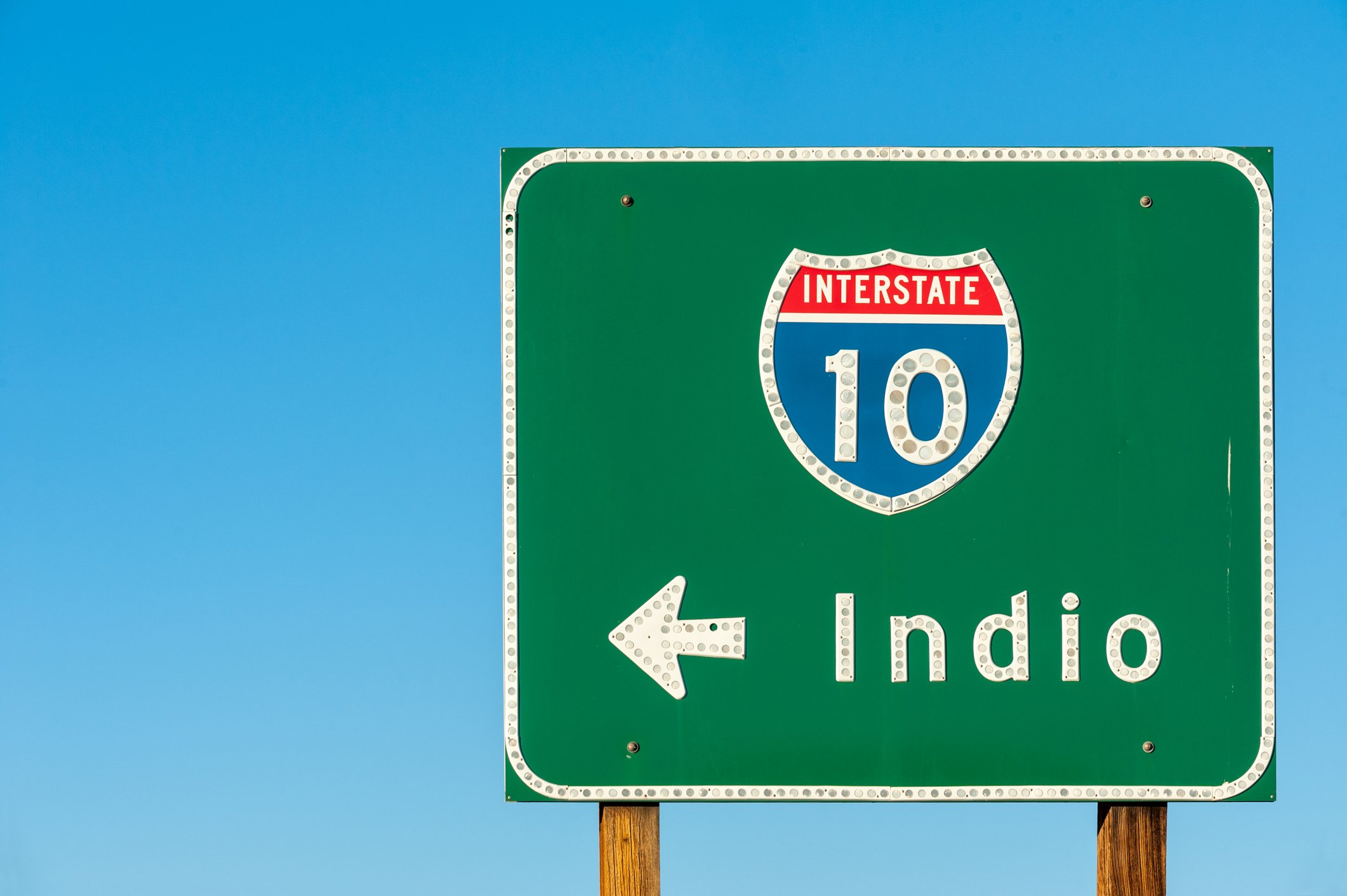 Directional road sign pointing toward Indio, set against a desert landscape with open skies and distant mountains—marking the gateway to California’s festival and desert escape scene. Book your Indio milestone or desert photography session today.