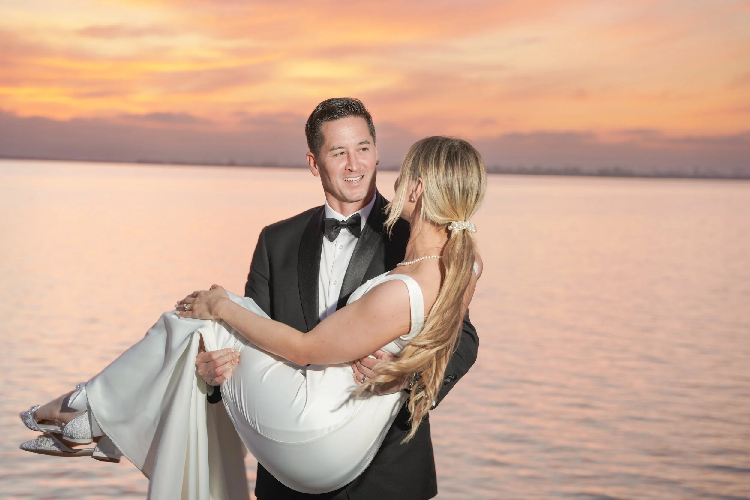 Groom Holding Bride at the Marina During Post-Wedding Portrait Session