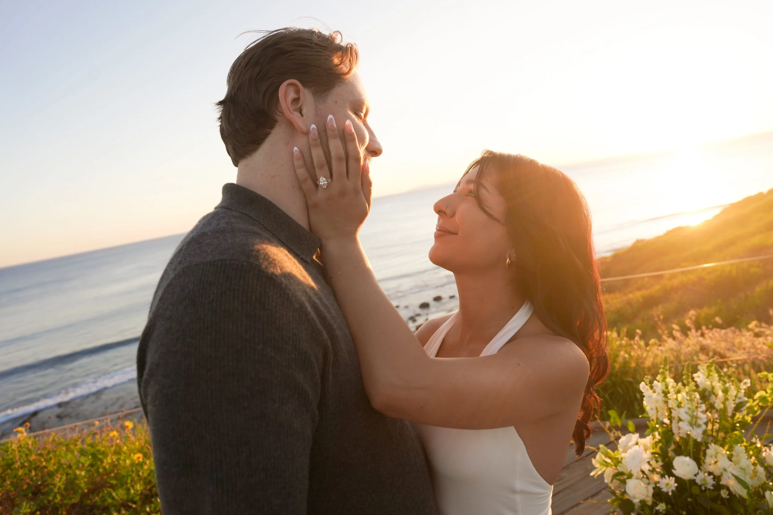 Fiancée holding her partner’s face after a surprise proposal at Crystal Cove State Beach, sharing an intimate post-engagement moment.