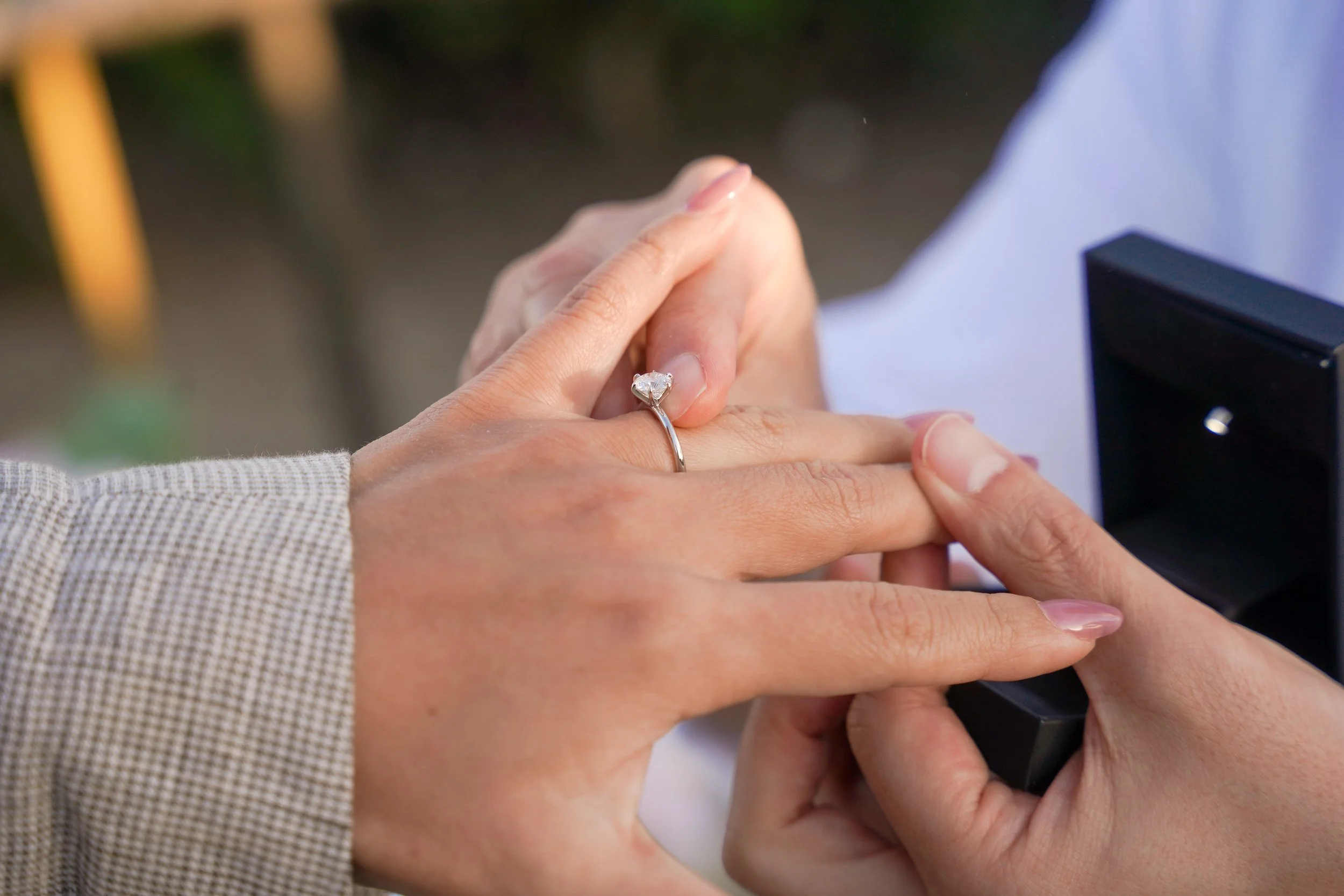 Client sliding an engagement ring onto his fiancée’s finger after a surprise proposal at Crescent Bay Park in Laguna Beach during Memorial Day sunset.