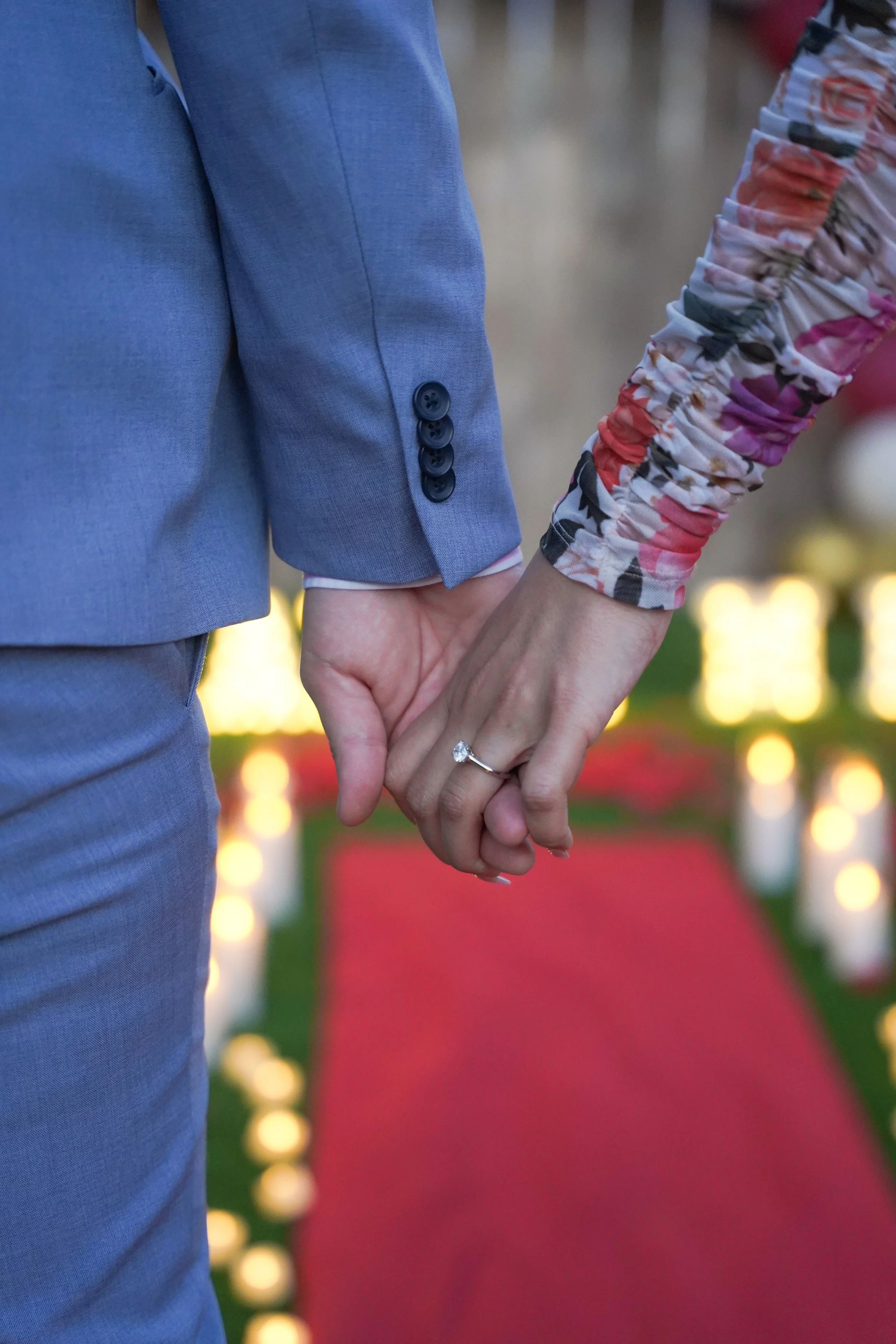 Couple holding hands with the San Diego at-home proposal décor softly blurred in the background, capturing the intimate moment after the ring exchange.