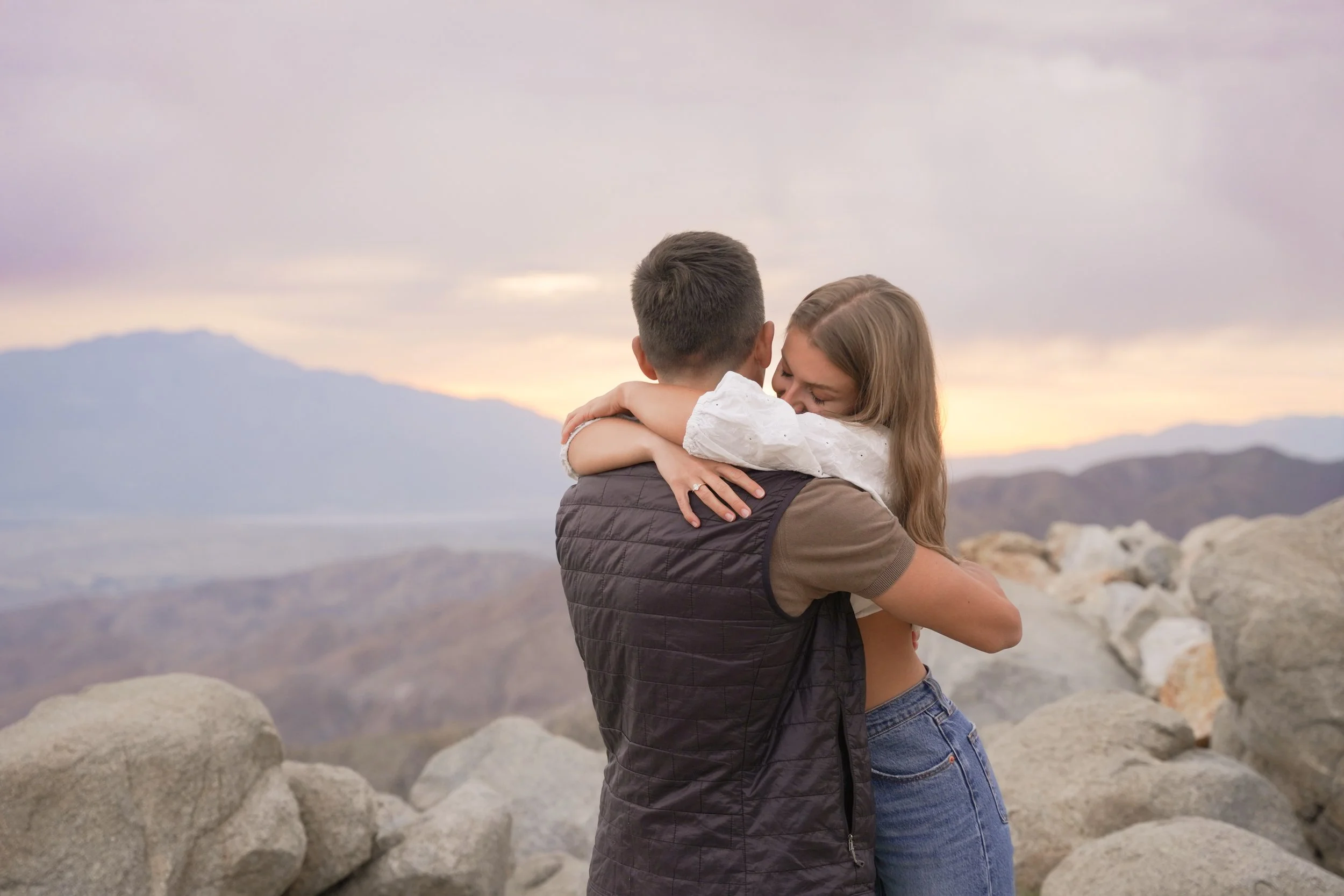 Couple embracing emotionally after surprise proposal at sunset, golden light surrounding them as they celebrate their engagement, captured by professional surprise proposal photographer.