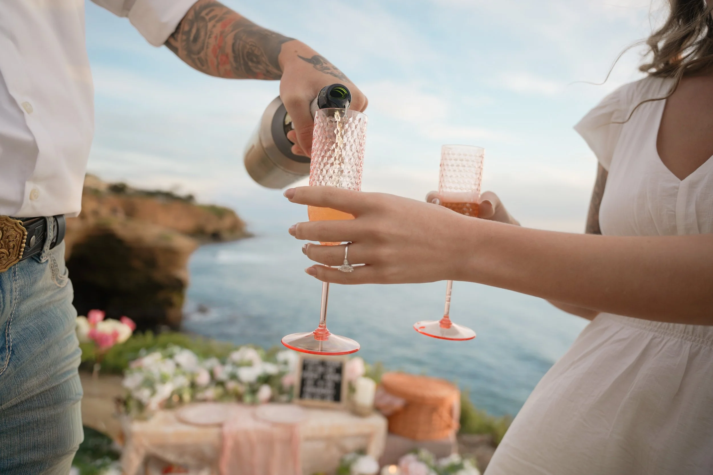 Newly engaged couple celebrating their surprise proposal with their first toast at Sunset Cliffs in San Diego as the sun sets over the Pacific, captured by a surprise proposal photographer during a romantic coastal engagement session.