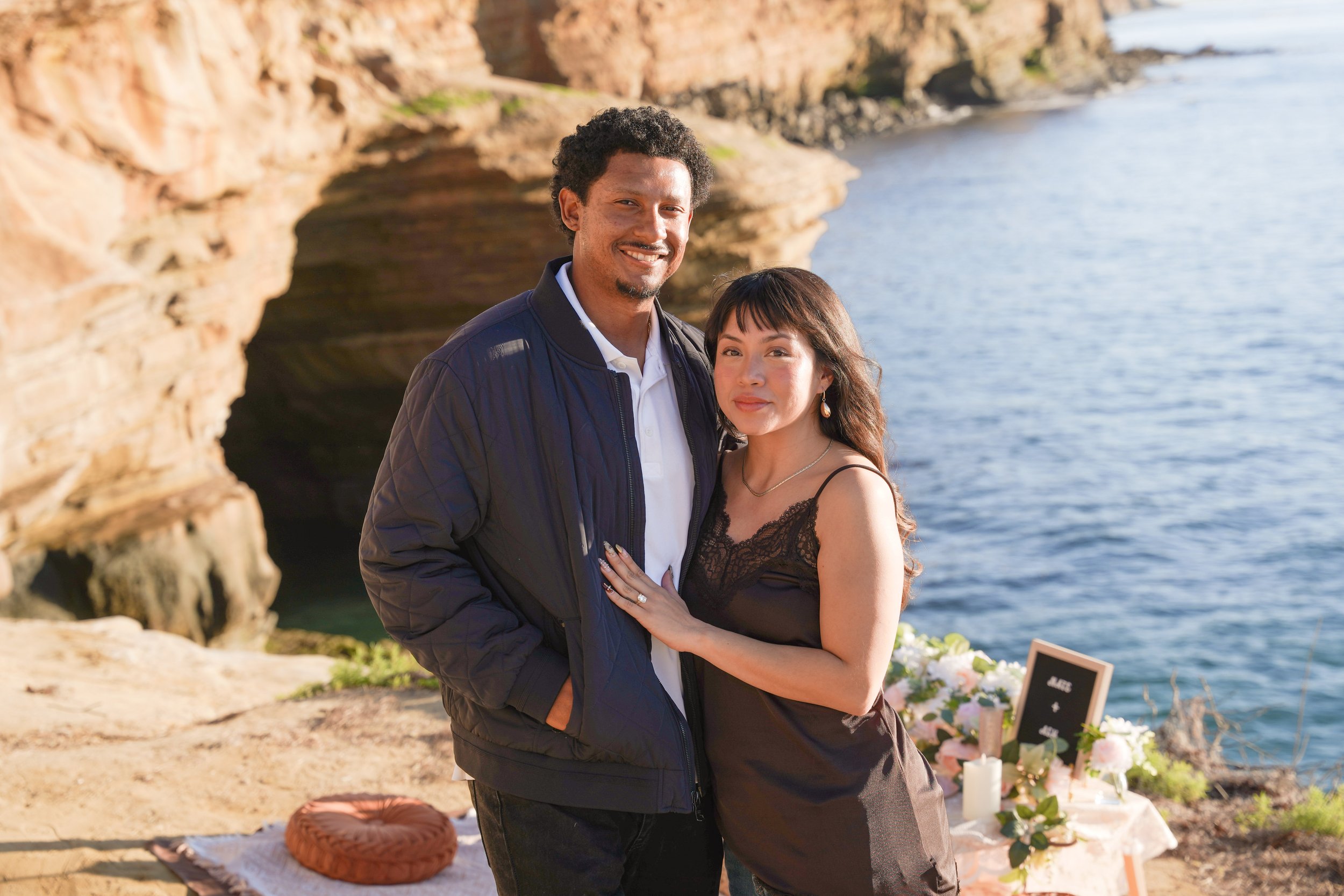 Luxury picnic surprise proposal at Sunset Cliffs, San Diego, capturing the emotional moment of Nate proposing to Ashley at sunset with an elevated, curated coastal picnic setup overlooking the ocean.