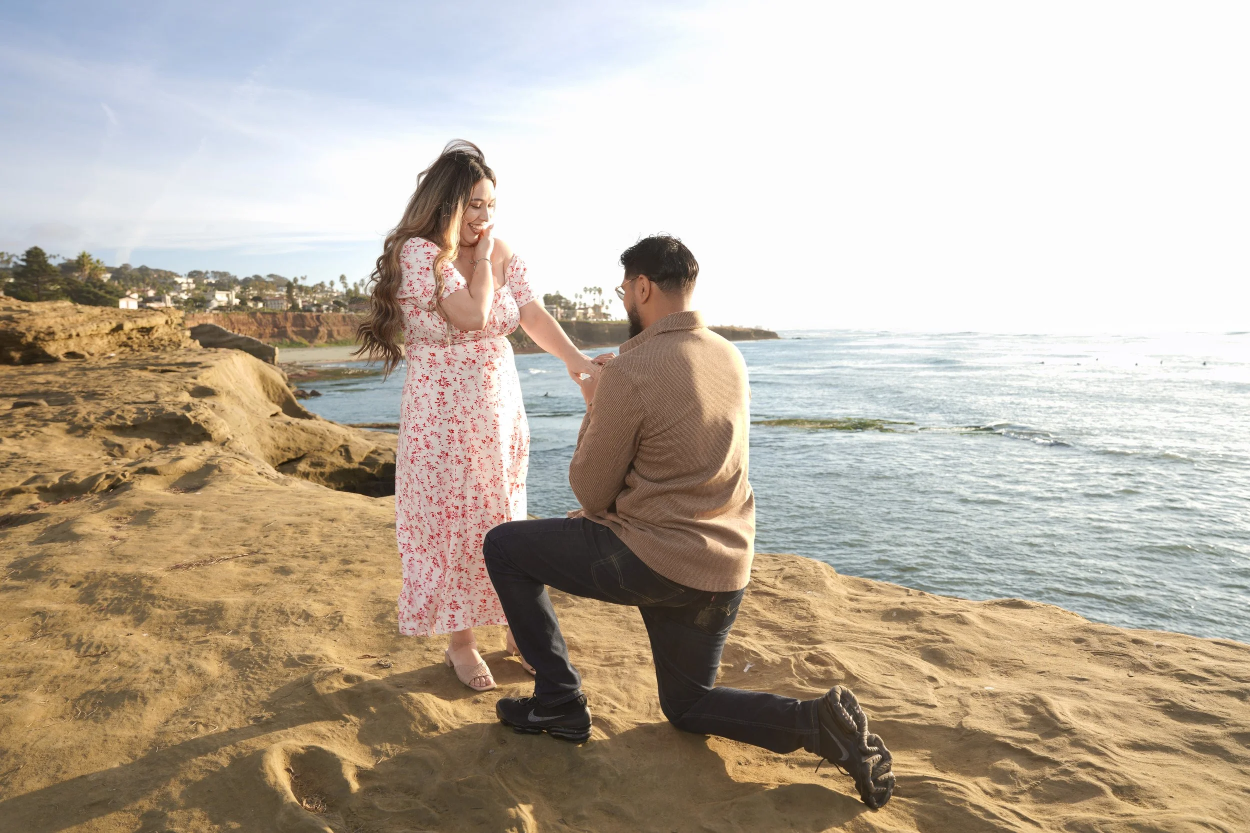 Surprise proposal at Sunset Cliffs in San Diego captured during golden hour as the groom-to-be drops to one knee overlooking the Pacific Ocean