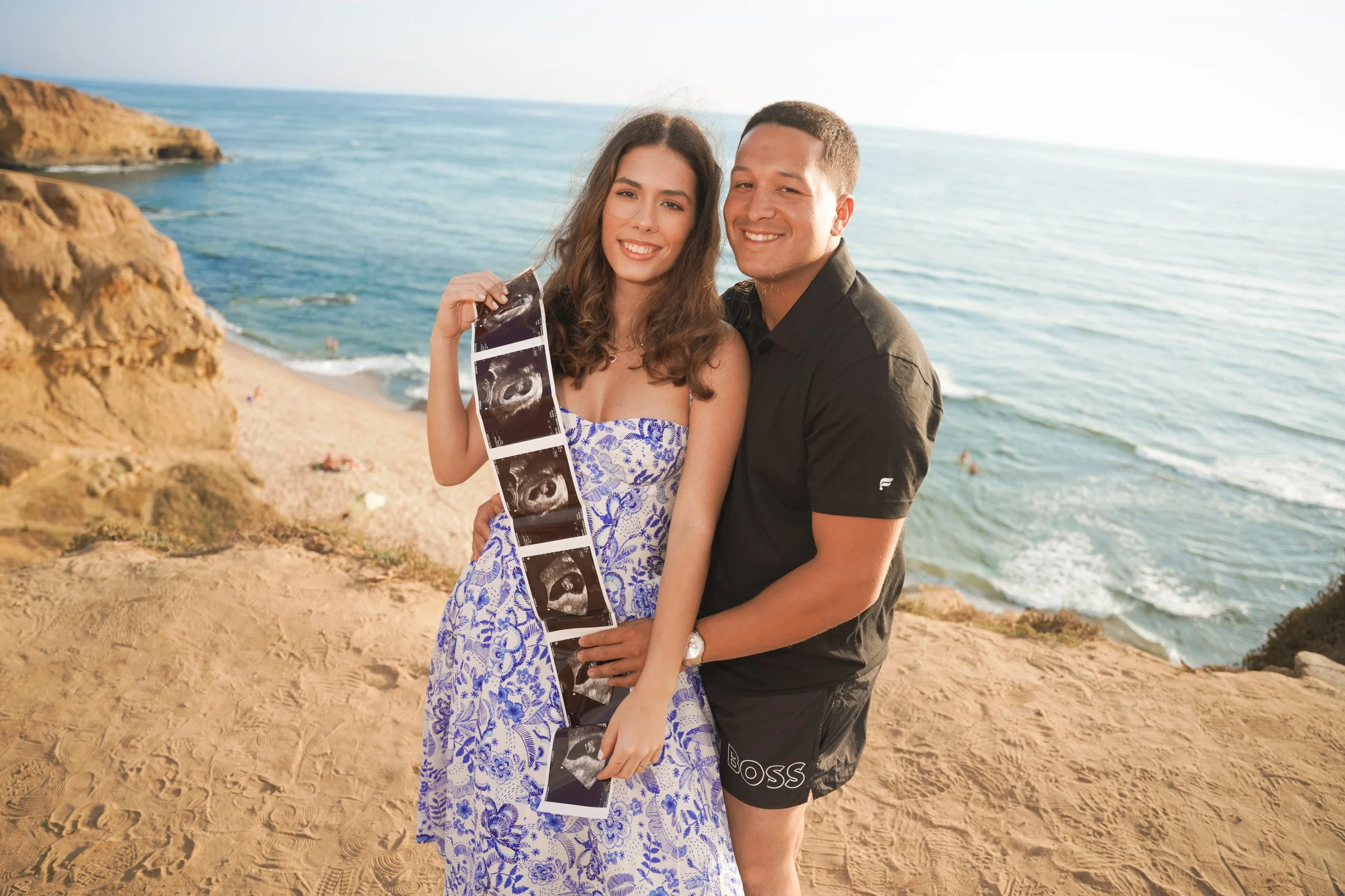 San Diego pregnancy reveal photoshoot at Sunset Cliffs beach as the sun sets over the Pacific Ocean with golden light and timeless beauty, schedule your professional announcement photography now.