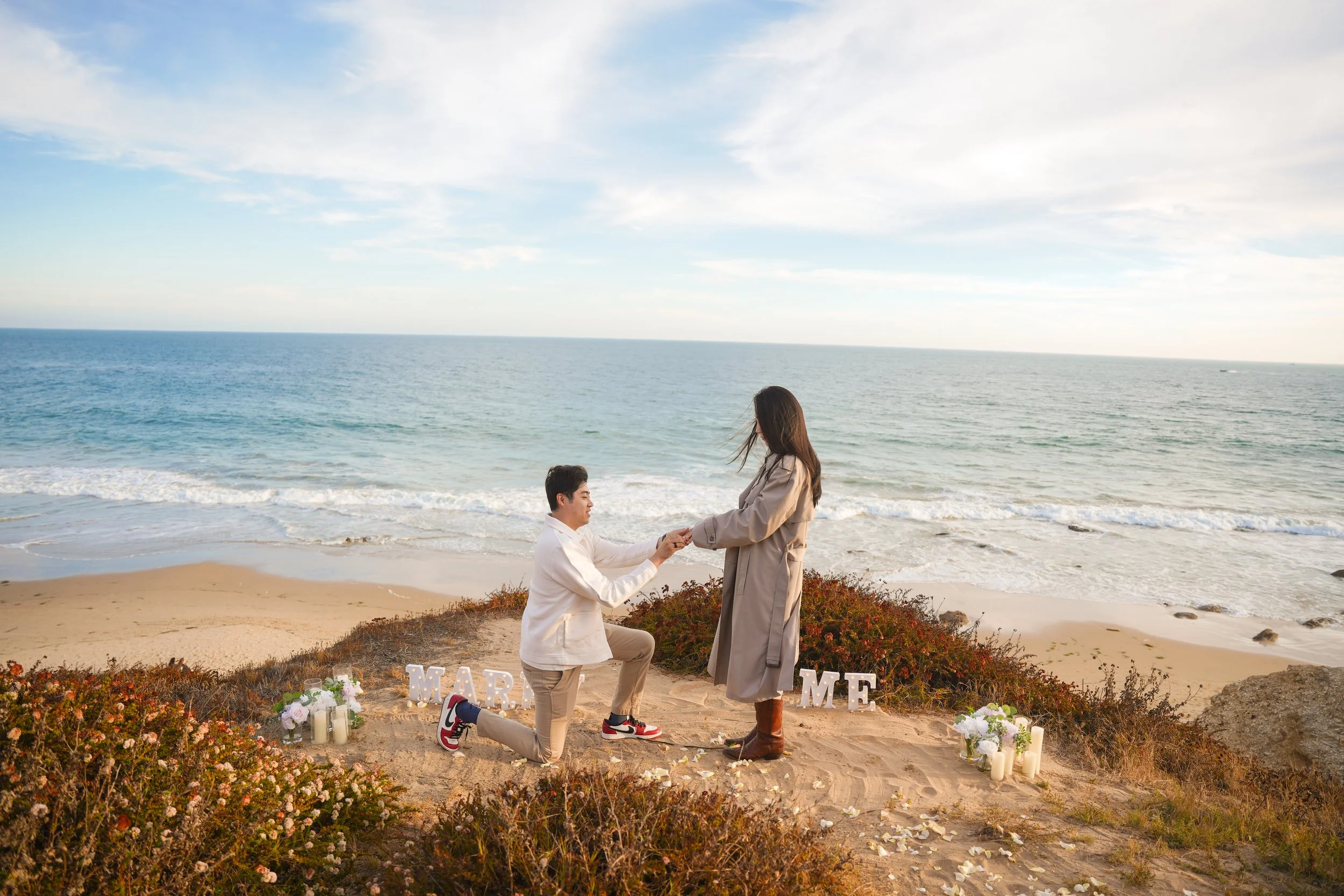 Luxury Newport Beach surprise proposal featuring our romantic setup with a 6-inch "Marry Me" sign, rose petals, elegant floral décor, and a breathtaking sunset overlooking the Pacific Ocean.