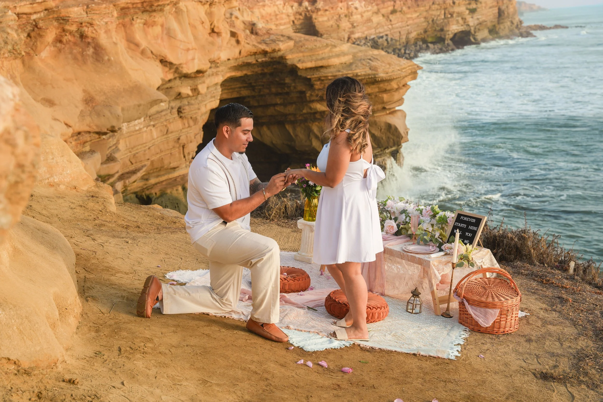 Romantic cliffside proposal at Sunset Cliffs in San Diego featuring our boho picnic proposal setup with Pacific Ocean views.