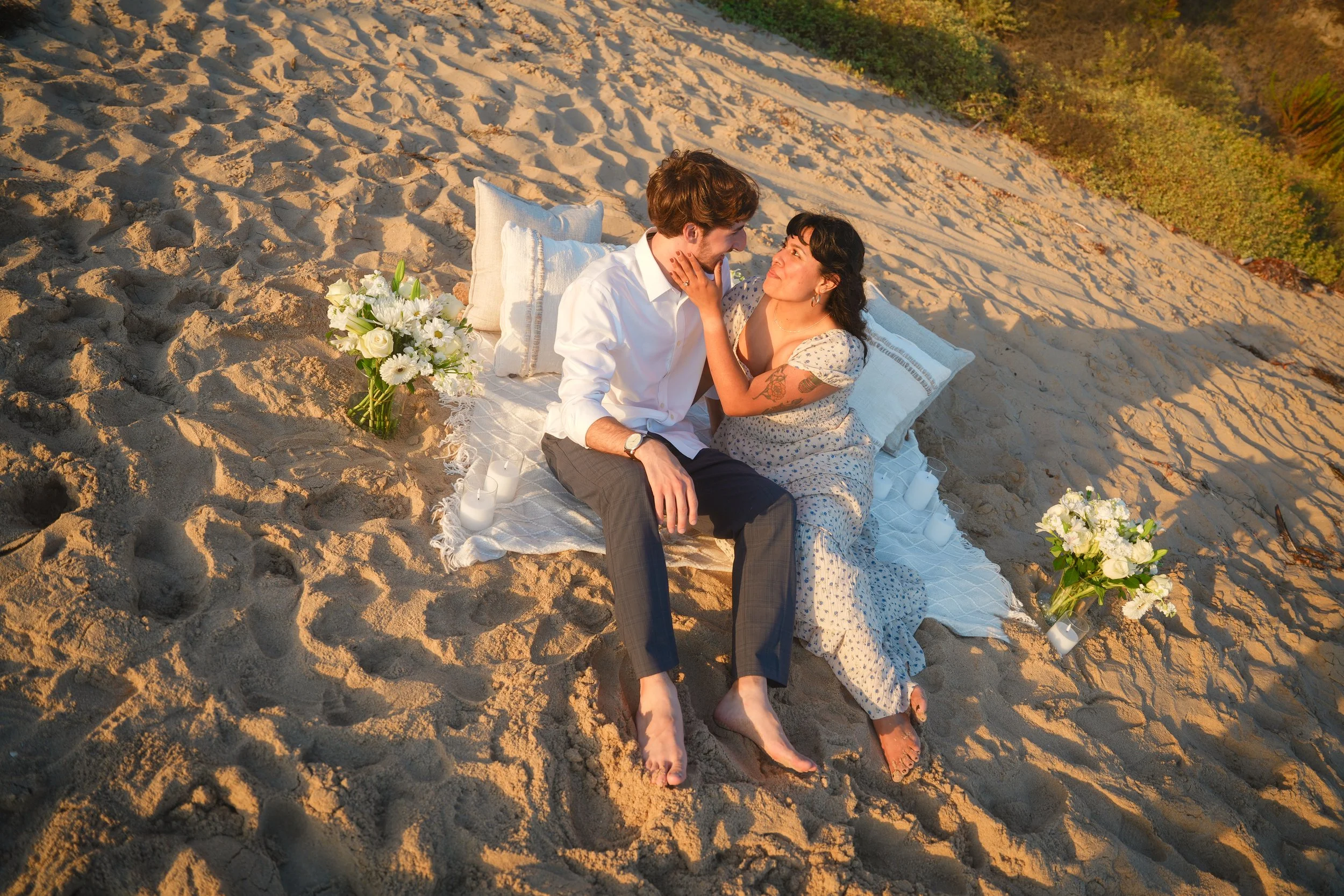 Minimal Laguna Beach sunset proposal picnic setup with decorative throw pillows, flowers and romantic ocean views.