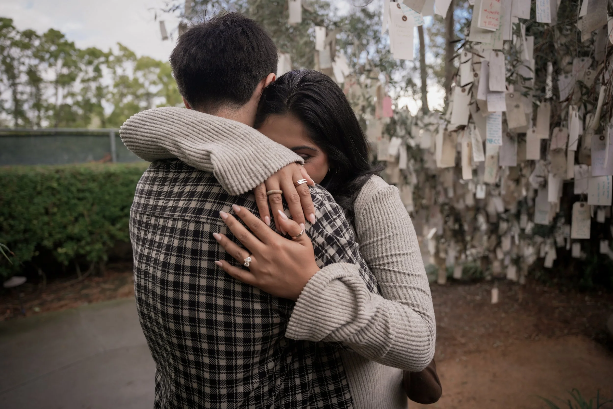 Couple embracing after their Estancia La Jolla proposal beneath the Wishing Tree, captured with warm tones and lush garden textures.