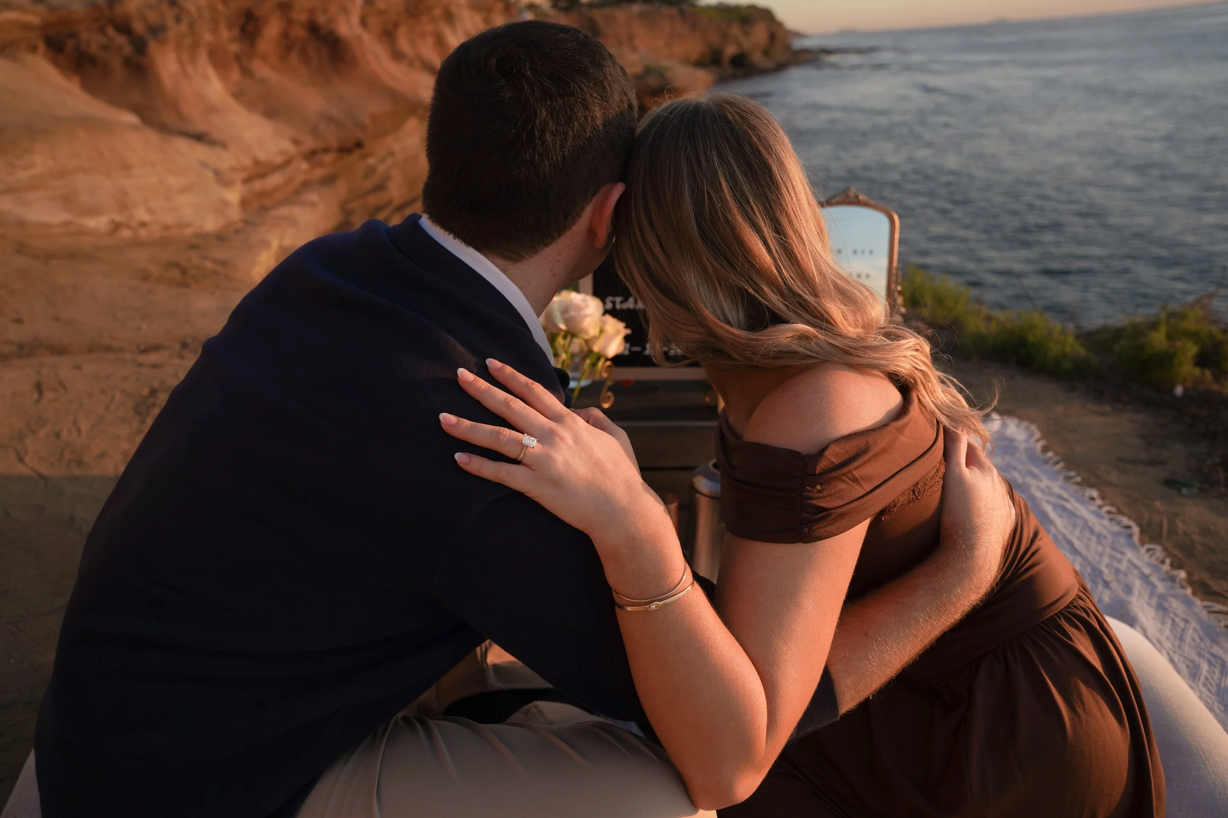 Golden hour surprise proposal at a Southern California beach with soft sunset light, ocean backdrop, and discreet proposal photography