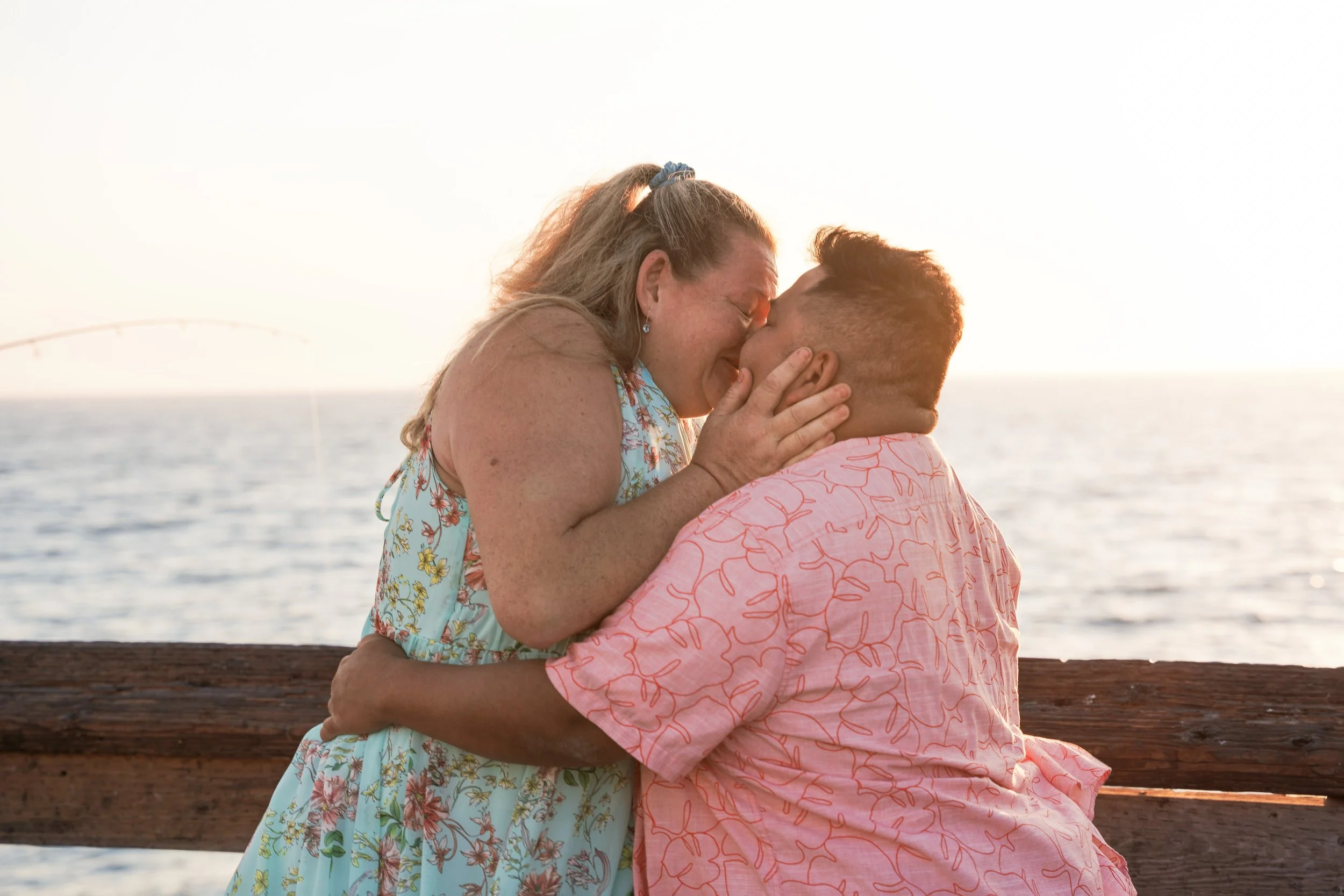 Undercover proposal photography in Newport Beach capturing Jennifer’s reaction as Miguel proposes on Balboa Pier during golden hour.