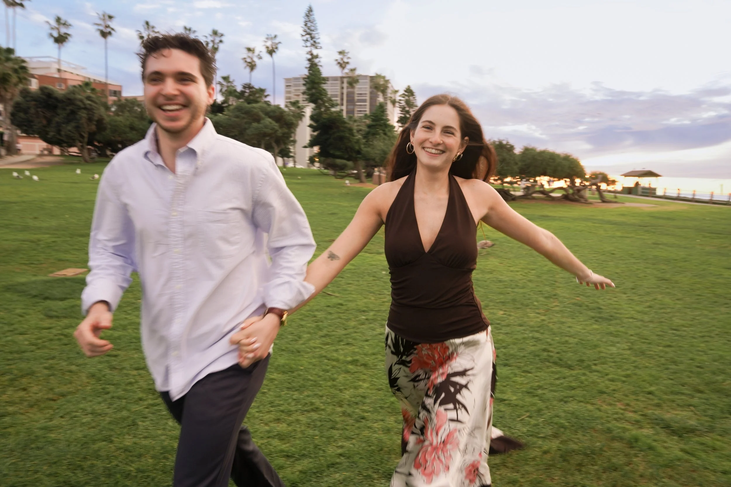Newly engaged couple running through Scripps Park at La Jolla Cove after proposal, candid coastal engagement photography capturing authentic reaction and movement