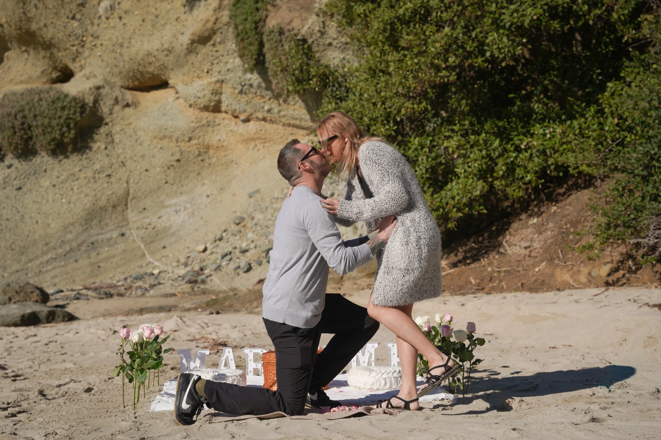 A real surprise proposal at Treasure Island Park in Laguna Beach, where Jeremy gets down on one knee to ask Jenny to marry him—planned and executed through our Marry Me picnic proposal package along the shoreline below Montage Resort.