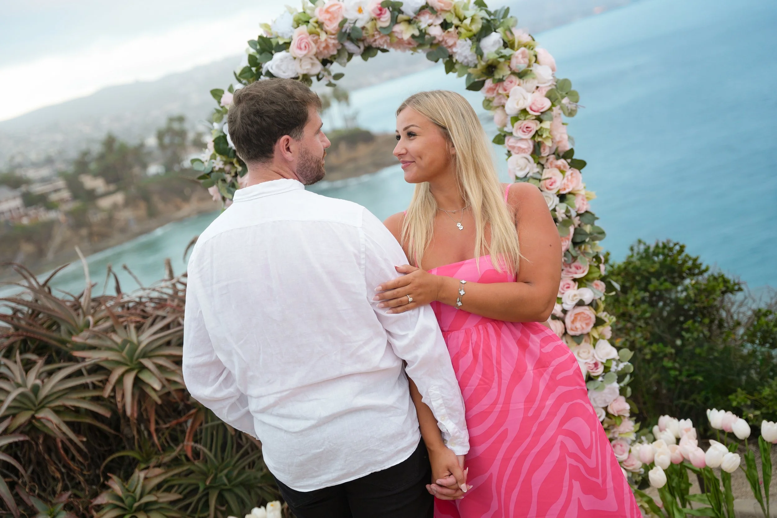 Romantic Laguna Beach engagement beneath our Signature Yes floral arch setup.